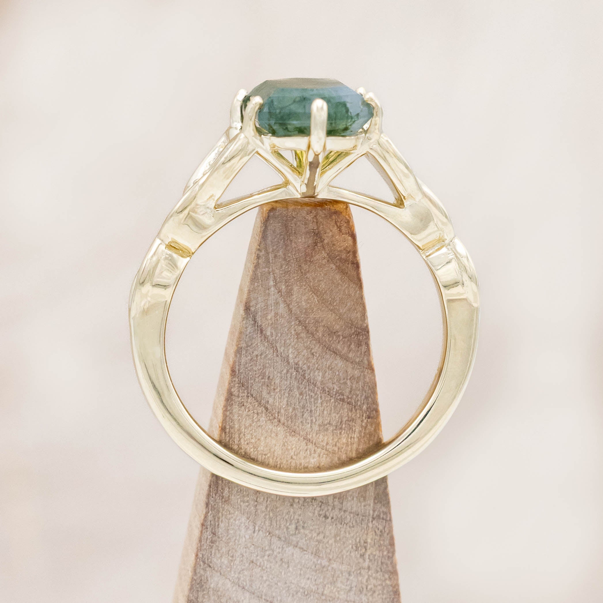 Gold ring with triquetra knot accent and moss agate on a wooden stand against a beige background