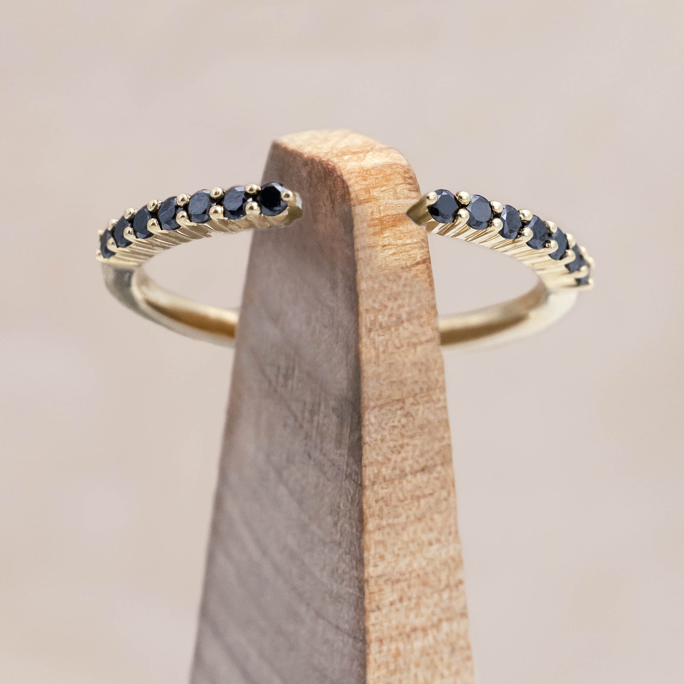 14K yellow gold ring with small black diamonds on a wooden stand against a beige background