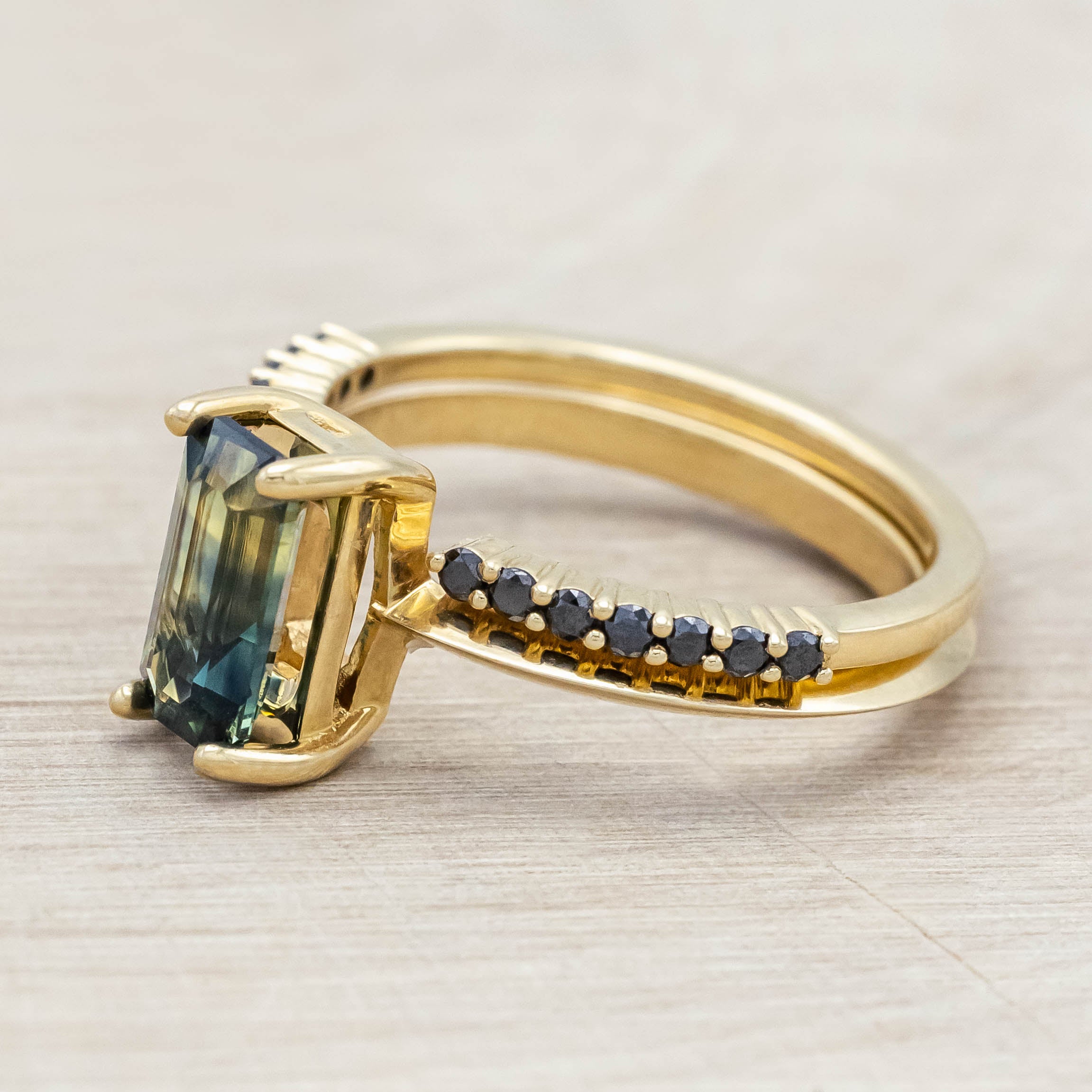 14K yellow gold ring with a green sapphire and black diamond tracer on a light wooden surface