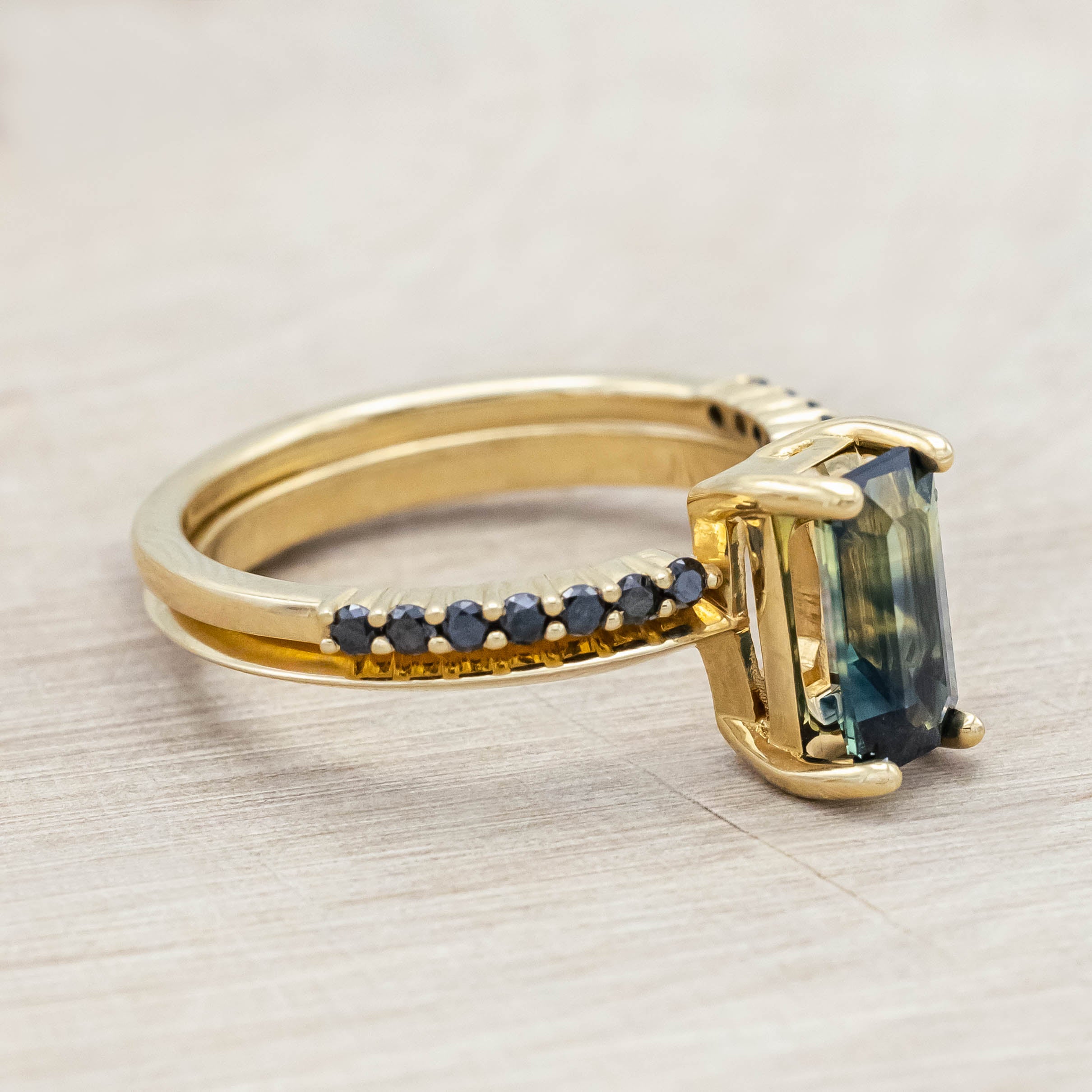 14K yellow gold ring with a green sapphire and black diamond tracer on a light wooden surface