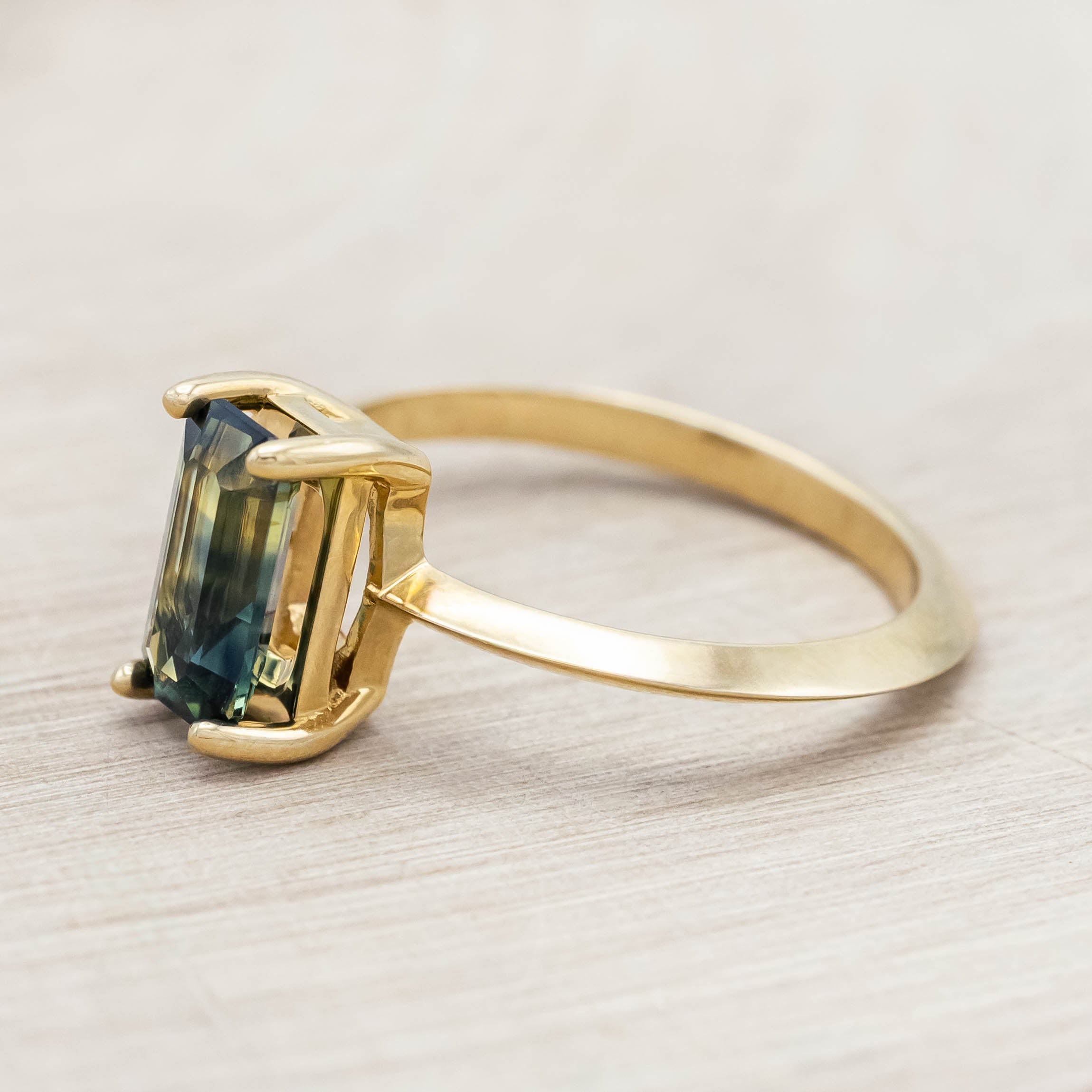 14K yellow gold ring with a green sapphire on a light wooden surface