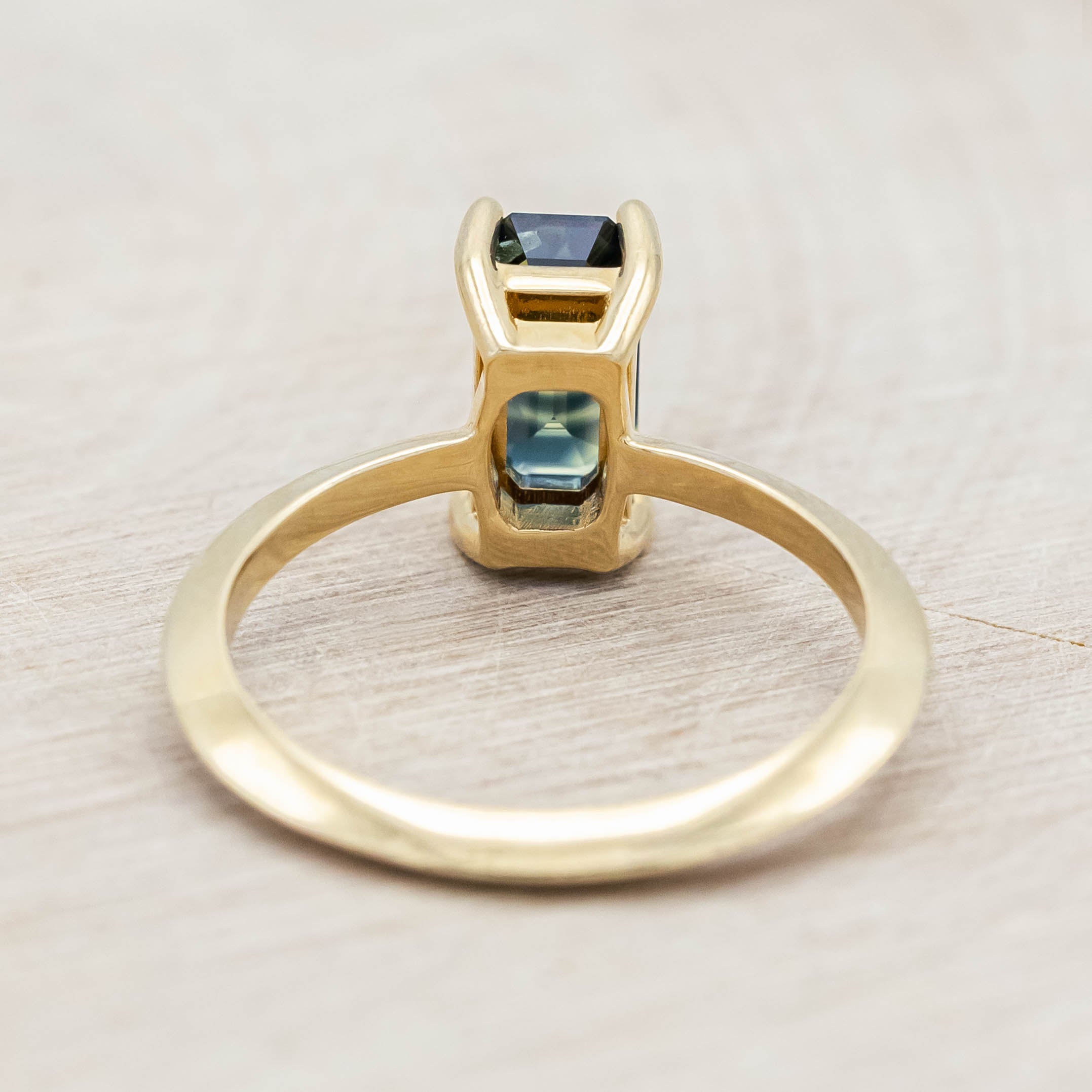 14K yellow gold ring with a green sapphire on a light wooden surface