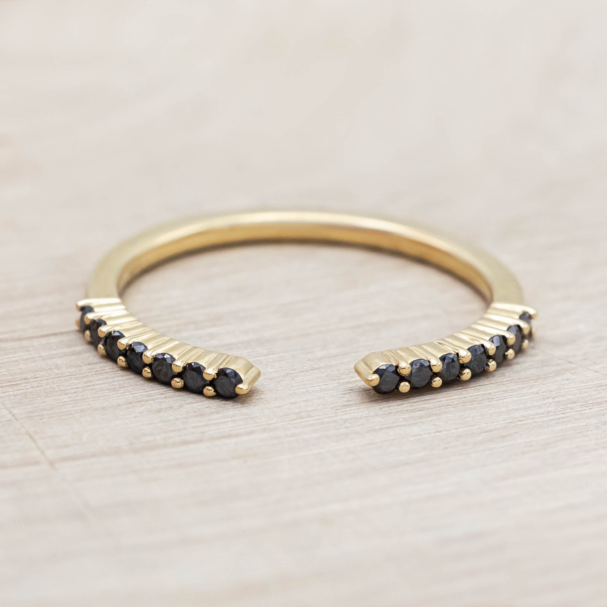 14K yellow gold ring with small black diamonds on a wooden stand against a beige background