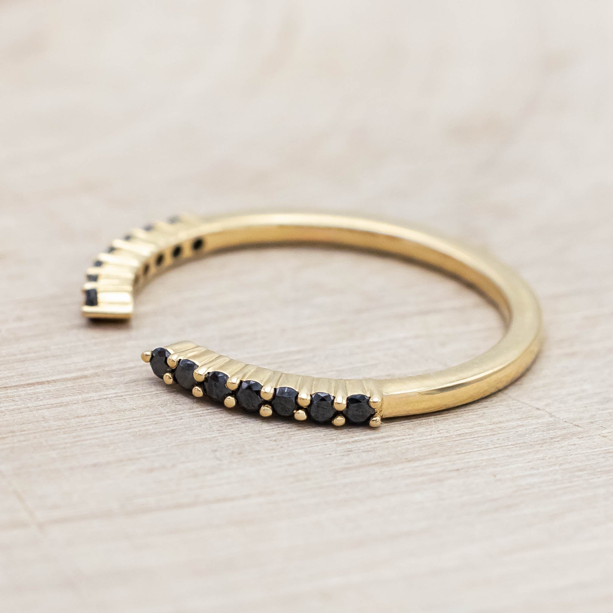 14K yellow gold ring with small black diamonds on a wooden stand against a beige background
