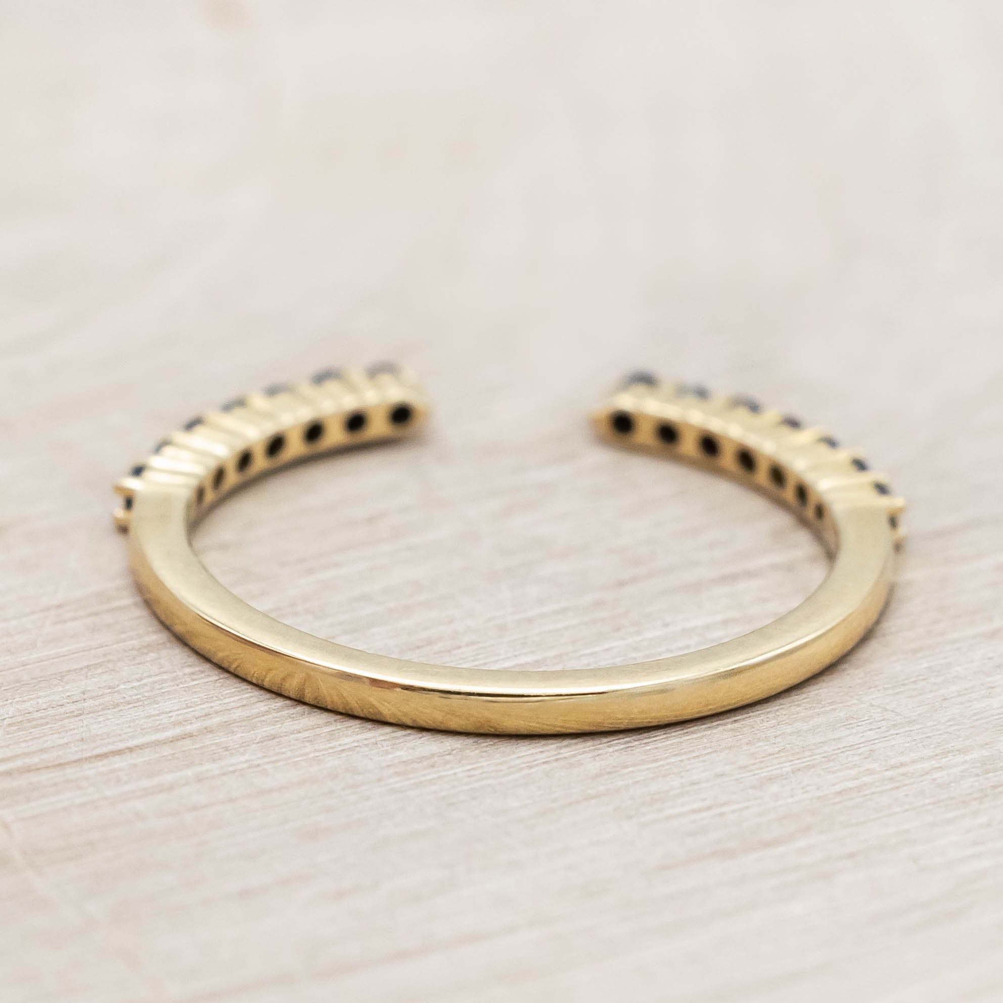 14K yellow gold ring with small black diamonds on a wooden stand against a beige background