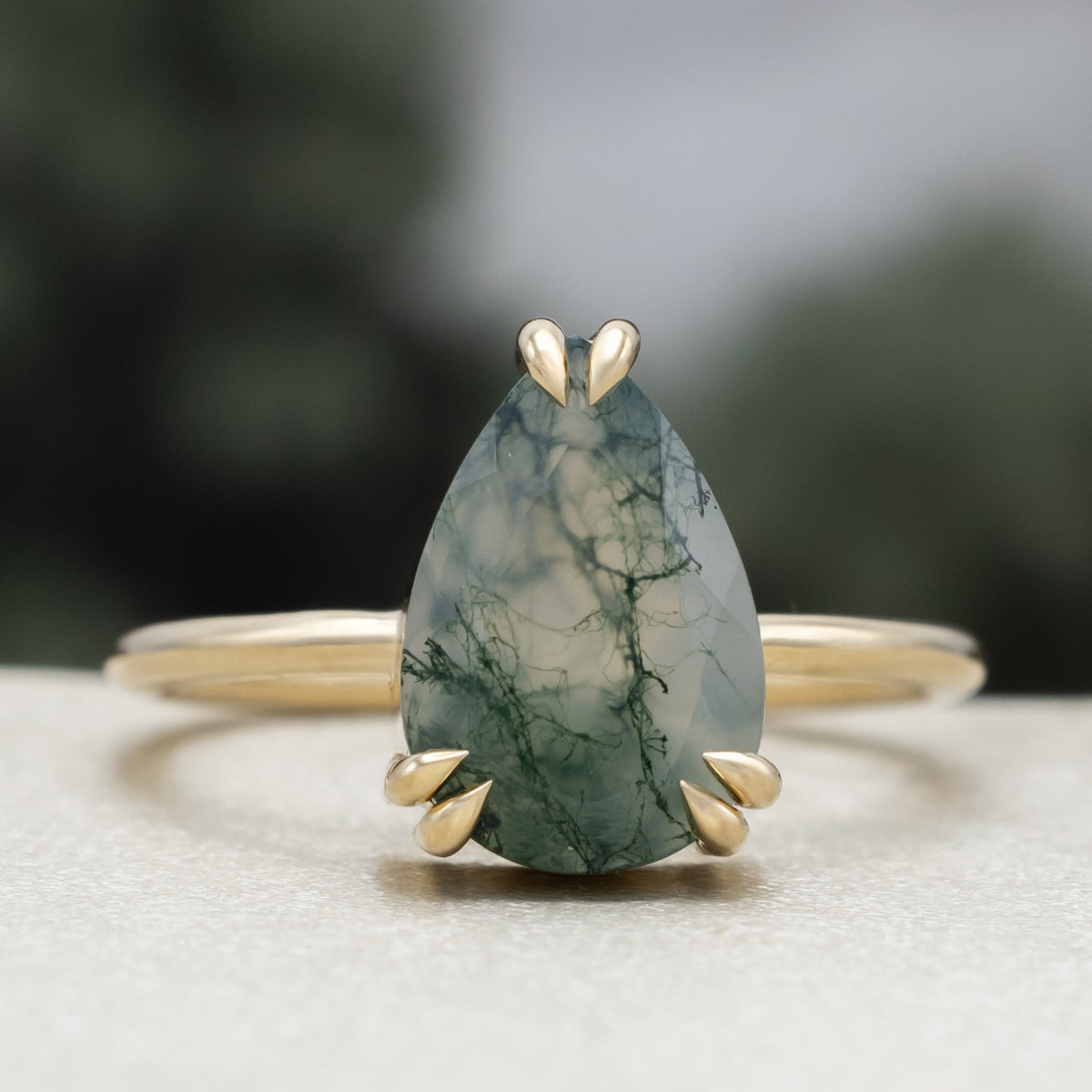 Gold ring with pear cut moss agate center stone against a blurred green background