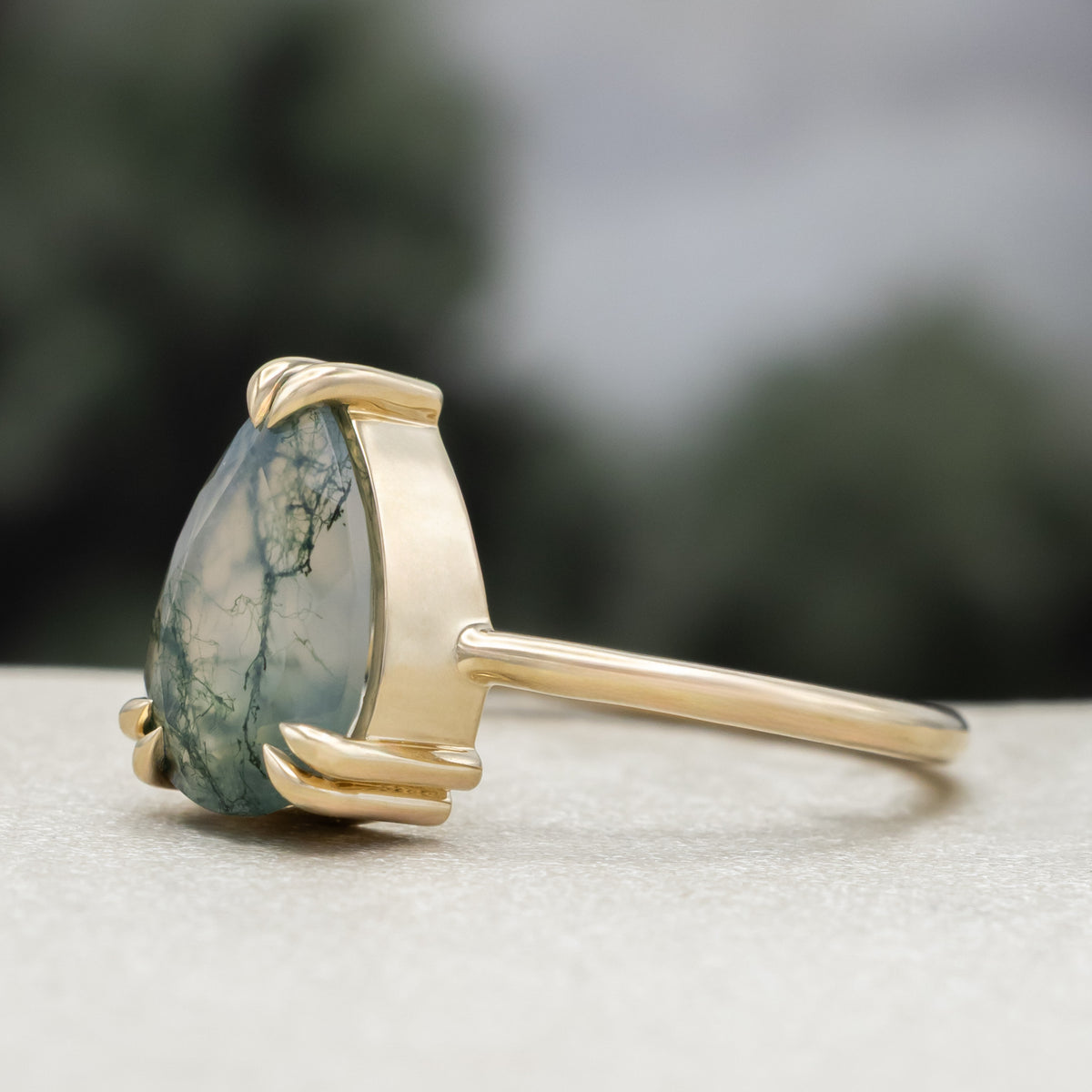 Gold ring with pear cut moss agate center stone against a blurred green background