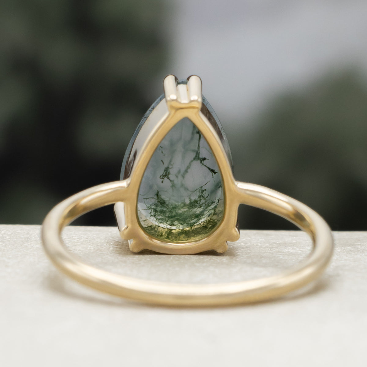 Gold ring with pear cut moss agate center stone against a blurred green background