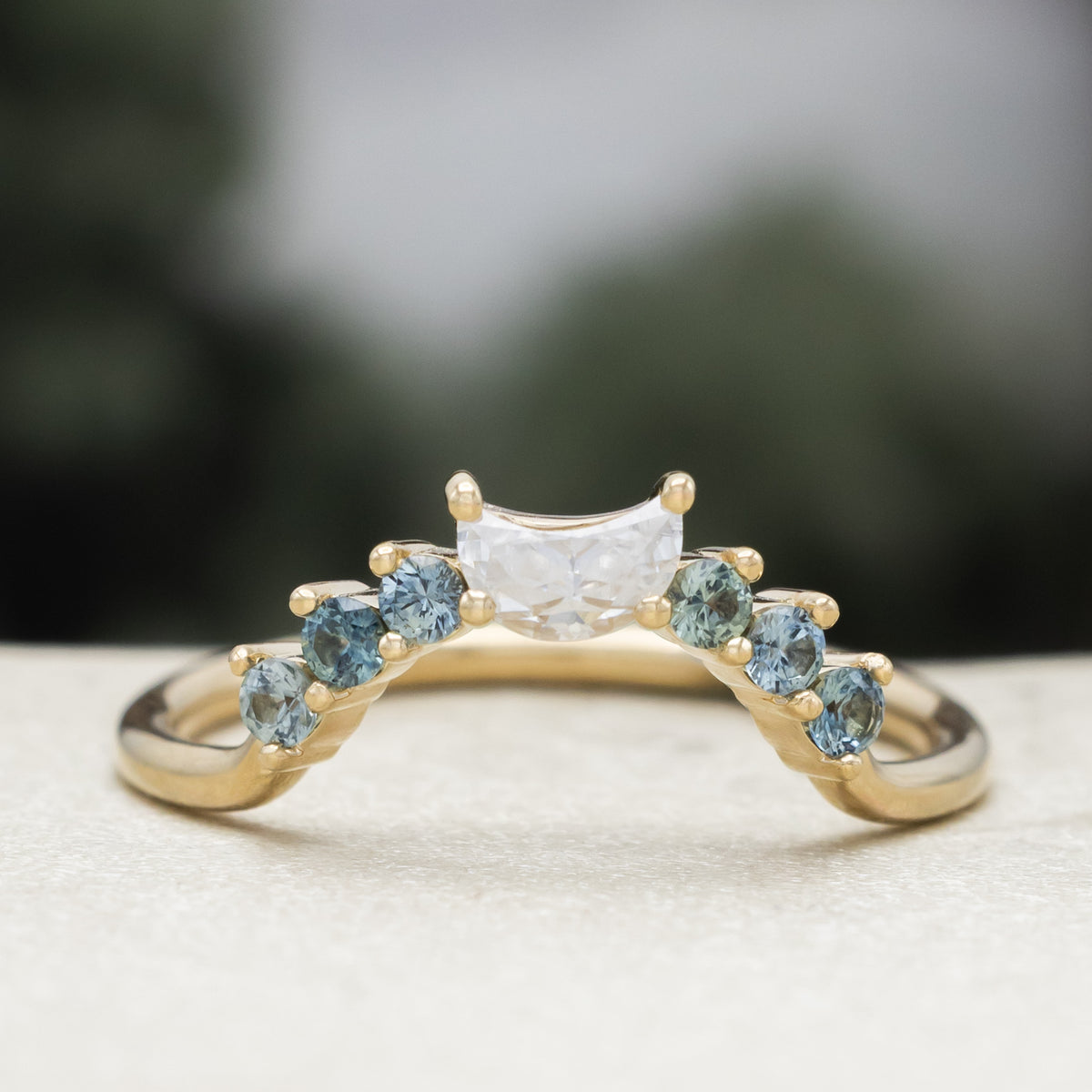 Gold ring tracer with moissanite and Montana sapphire accents against a blurred background