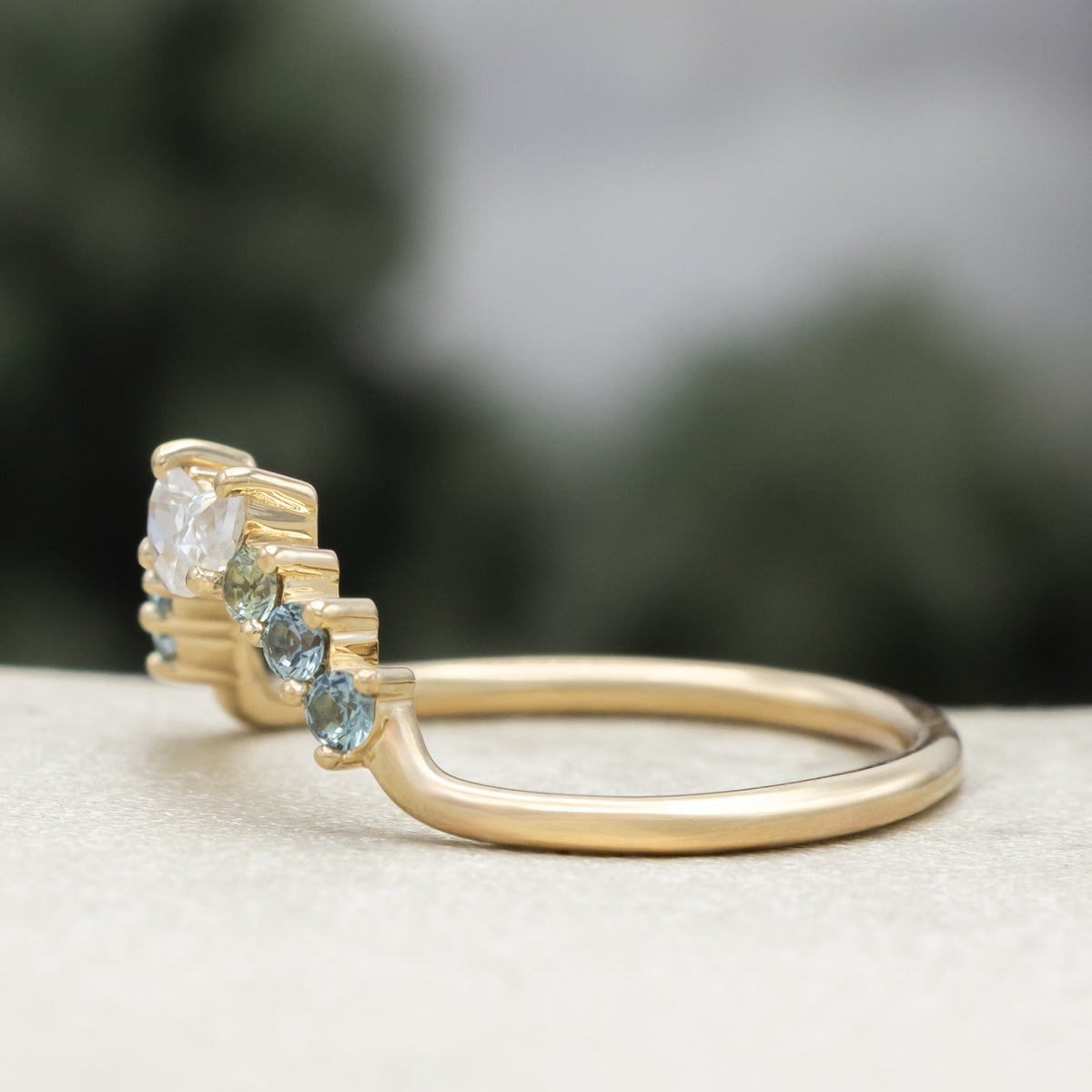 Gold ring tracer with moissanite and Montana sapphire accents against a blurred background
