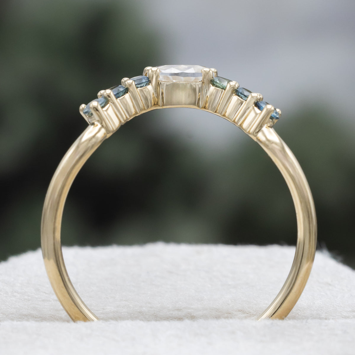 Gold ring tracer with moissanite and Montana sapphire accents against a blurred background