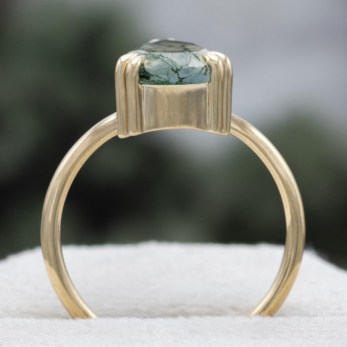 Gold ring with pear cut moss agate center stone against a blurred green background