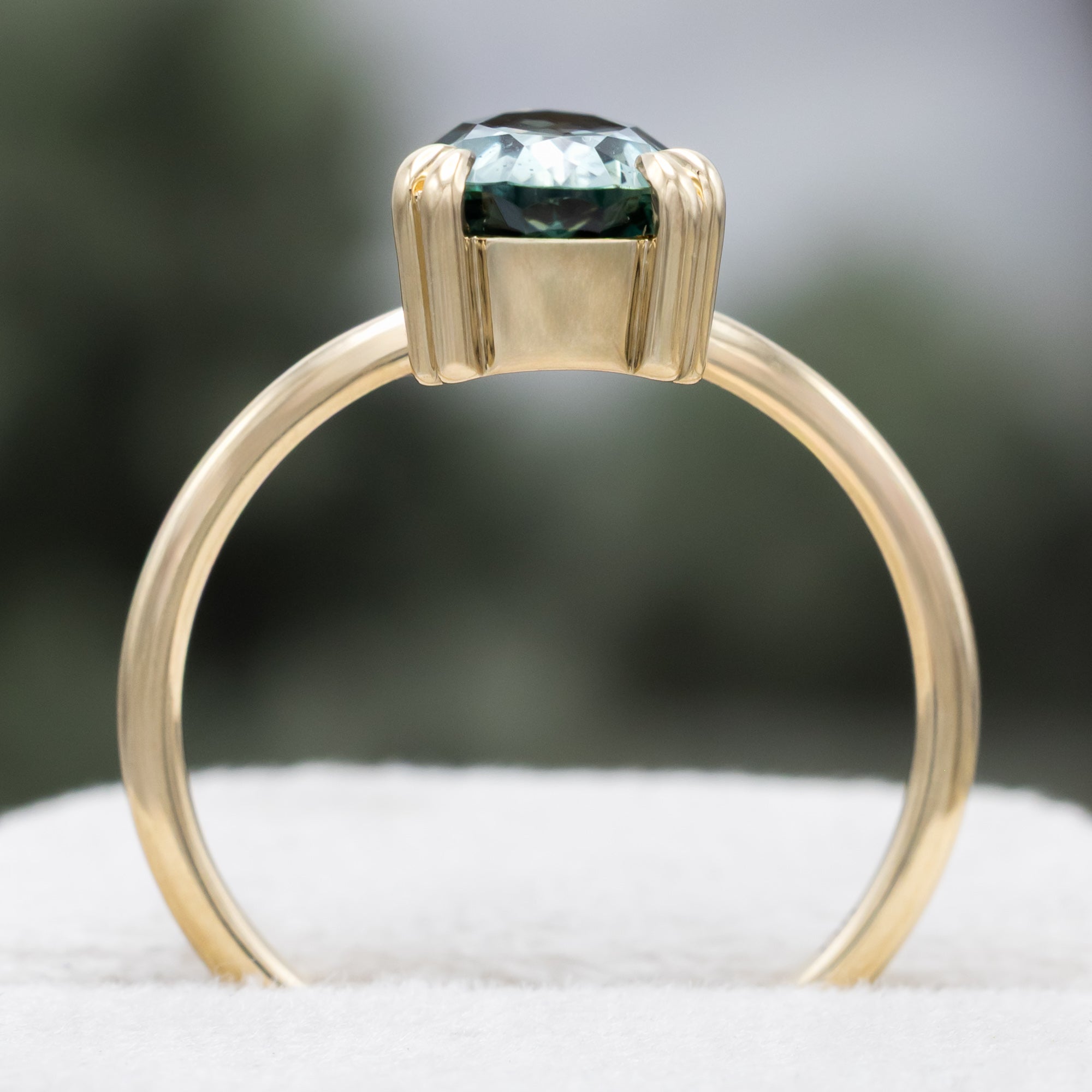 A solitaire gold ring featuring a pear-cut blue sapphire on a blurred green background.