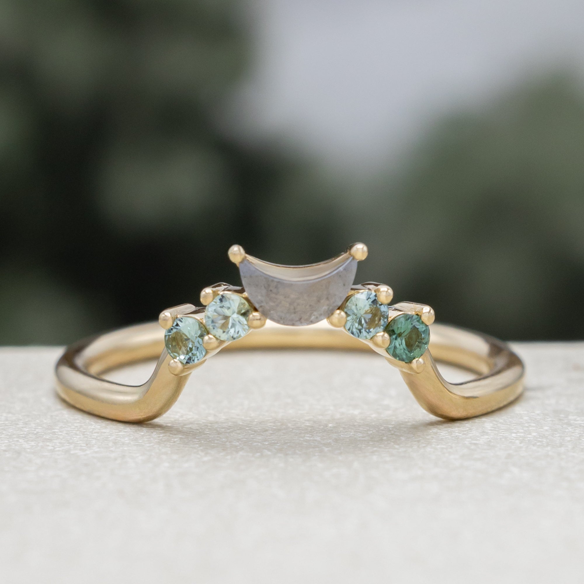 A gold ring tracer with round torumaline and crescent moon cut salt & pepper diamond on a blurred green background