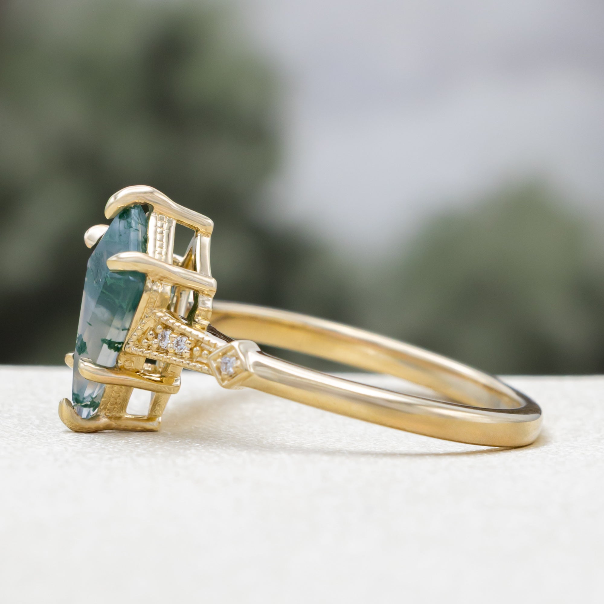 Gold ring with a moss agate centerstone & diamond accents on a blurred background