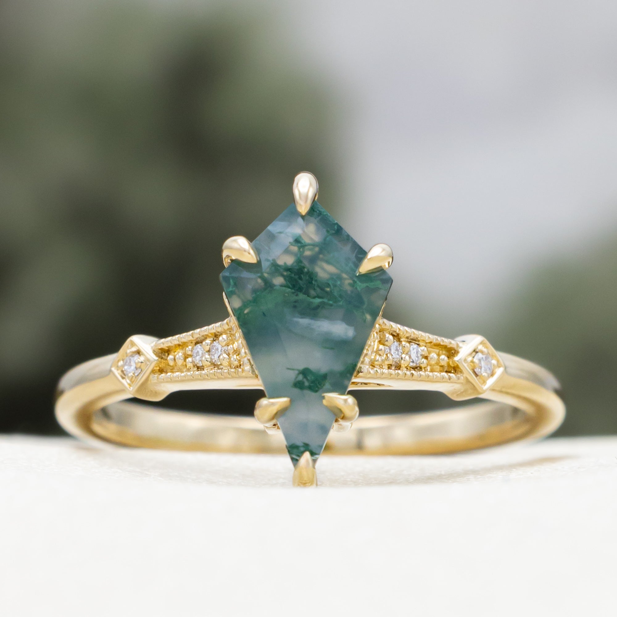Gold ring with a moss agate centerstone & diamond accents on a blurred background