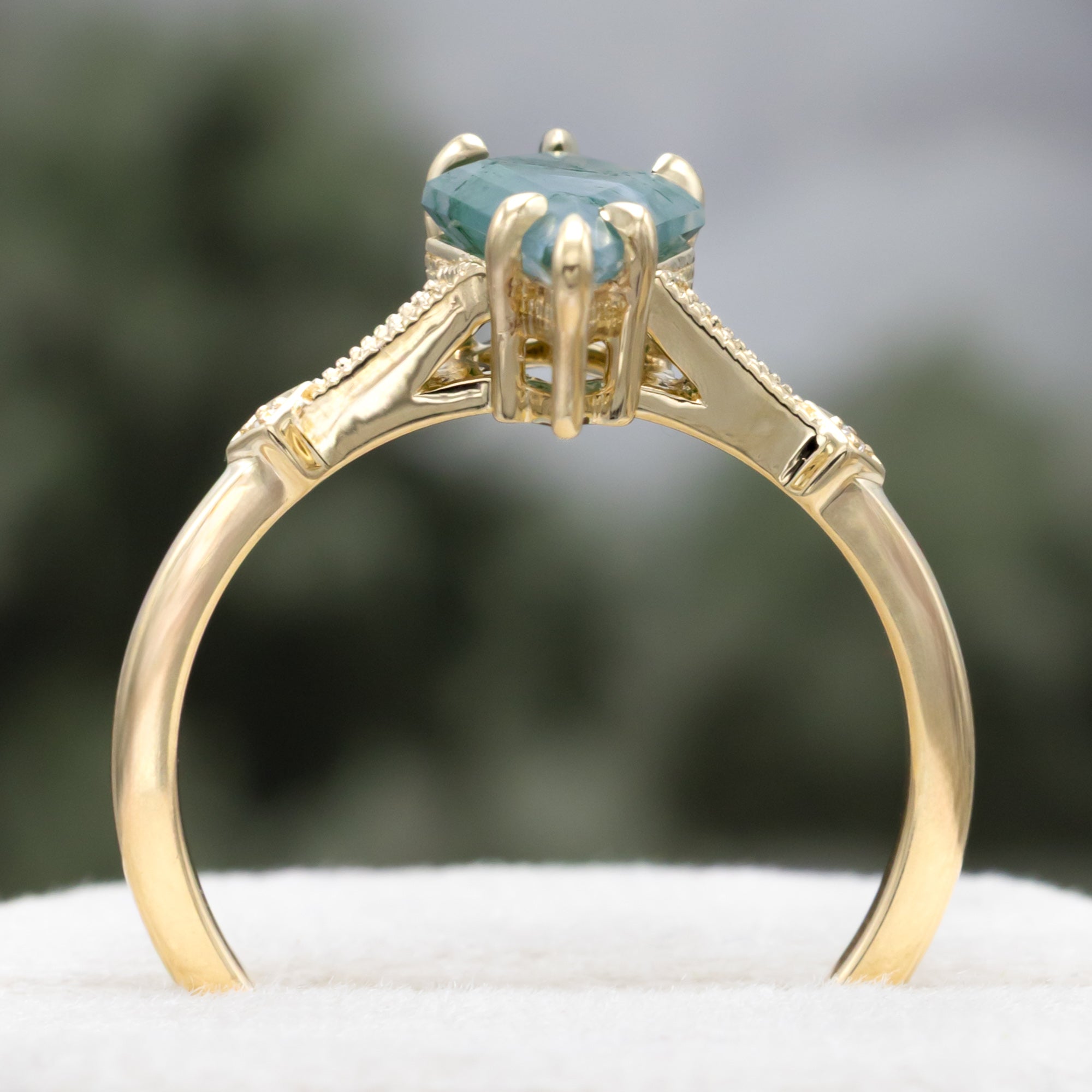 Gold ring with a moss agate centerstone & diamond accents on a blurred background