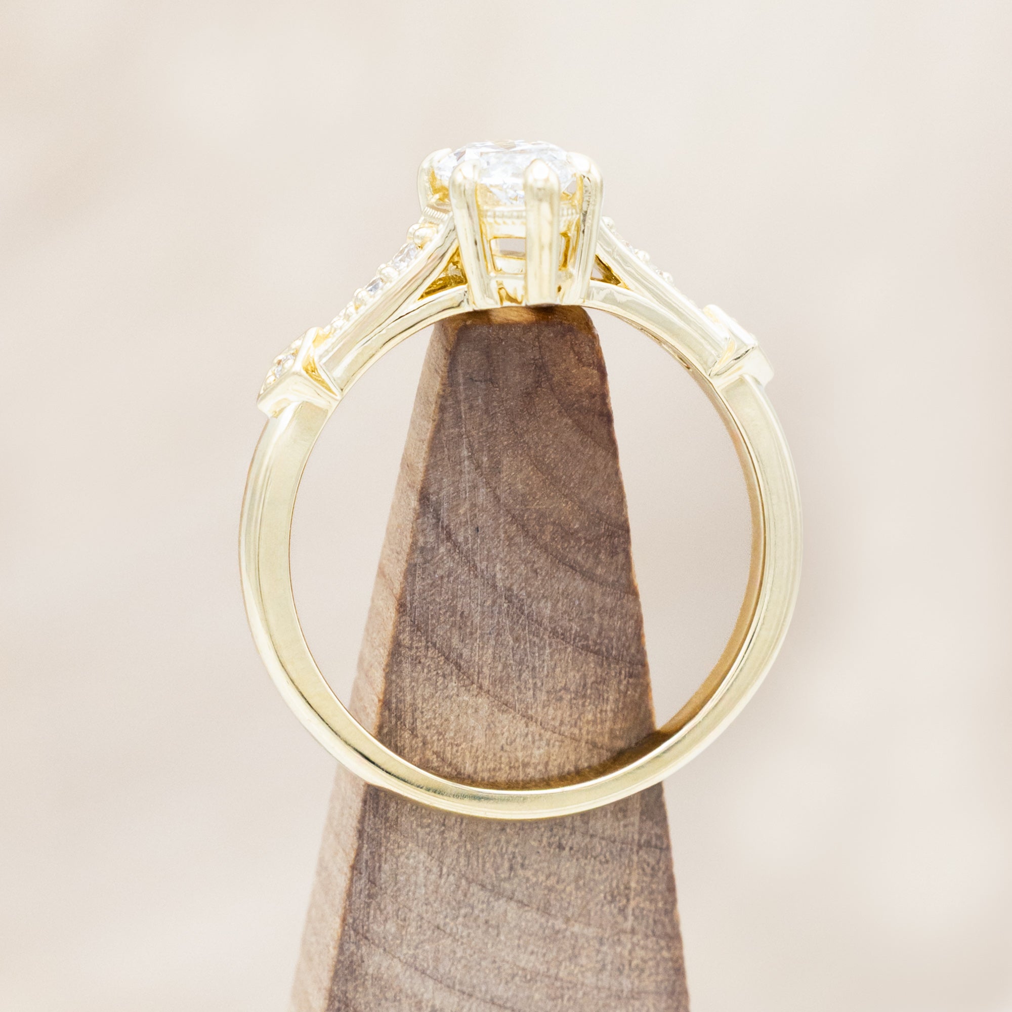 14K gold ring with lab-grown diamond center stone & accents on a wooden stand against a beige background