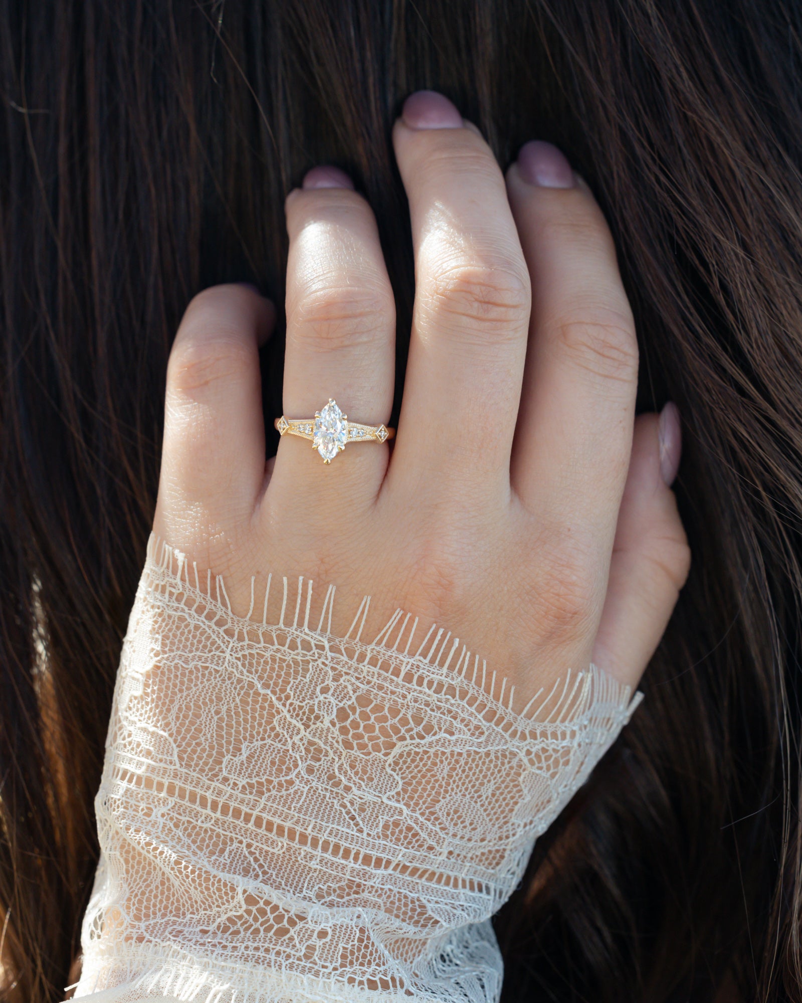 Hand wearing 14K gold ring with lab-grown diamond center stone & accents against dark hair