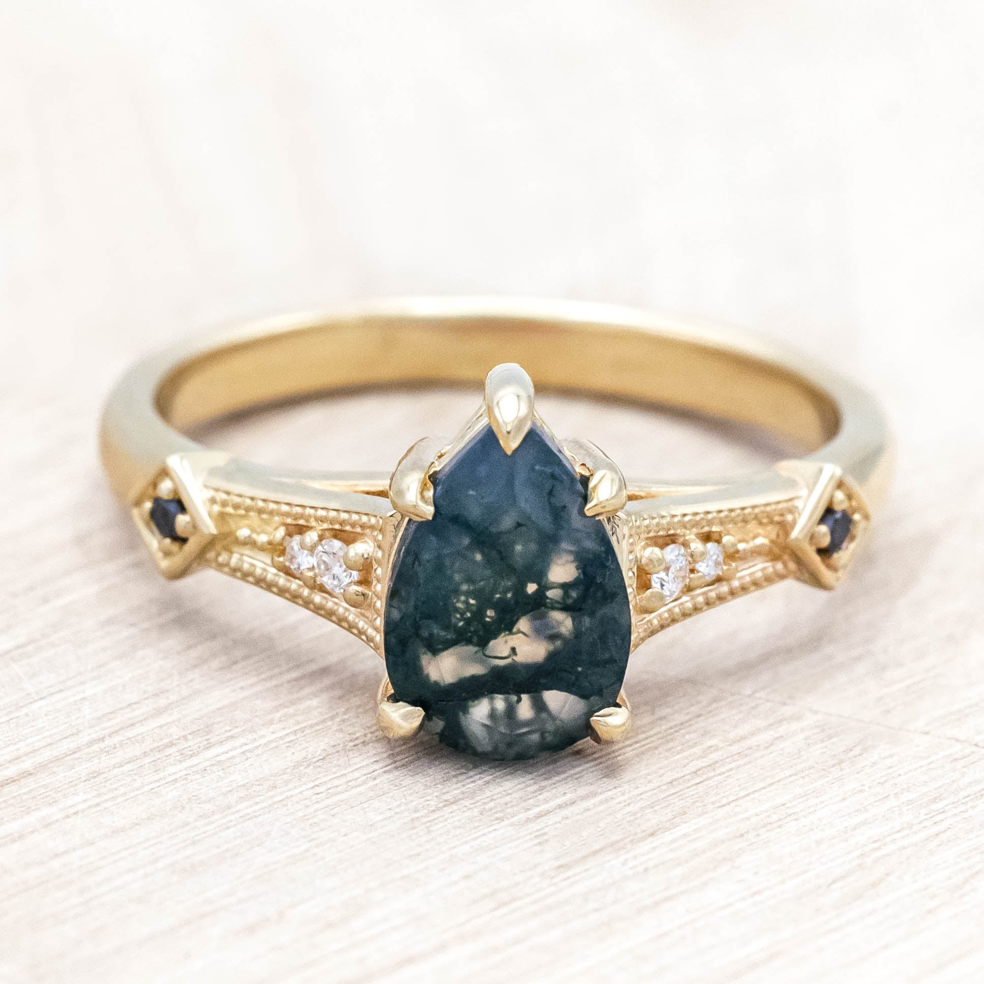 14K gold ring with a moss agate with black and white diamond accents on a wooden stand against a beige background