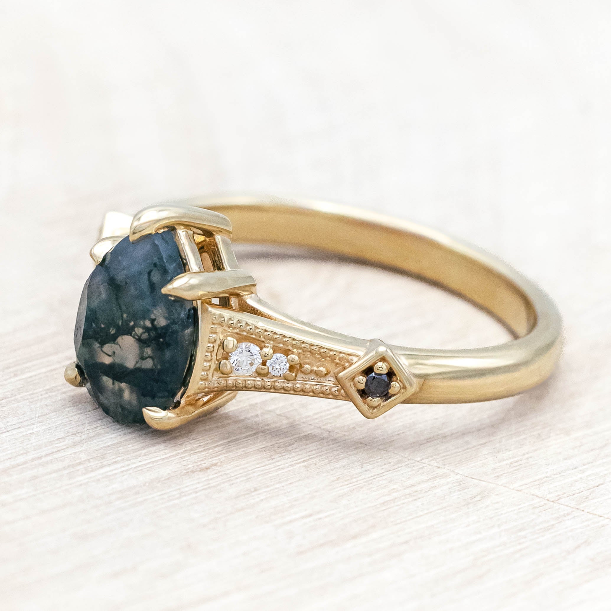 14K gold ring with a moss agate with black and white diamond accents on a wooden stand against a beige background