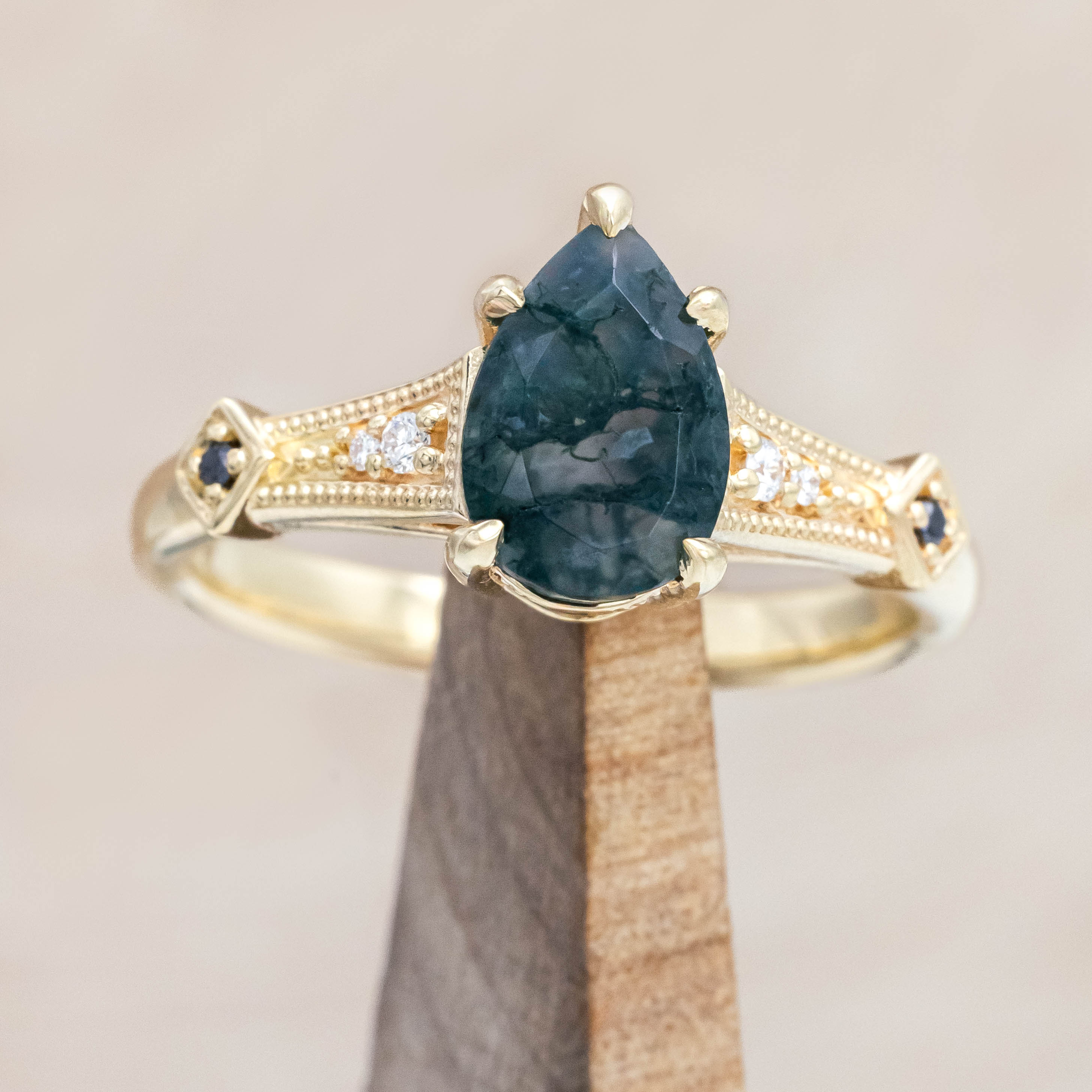 14K gold ring with a moss agate with black and white diamond accents on a wooden stand against a beige background