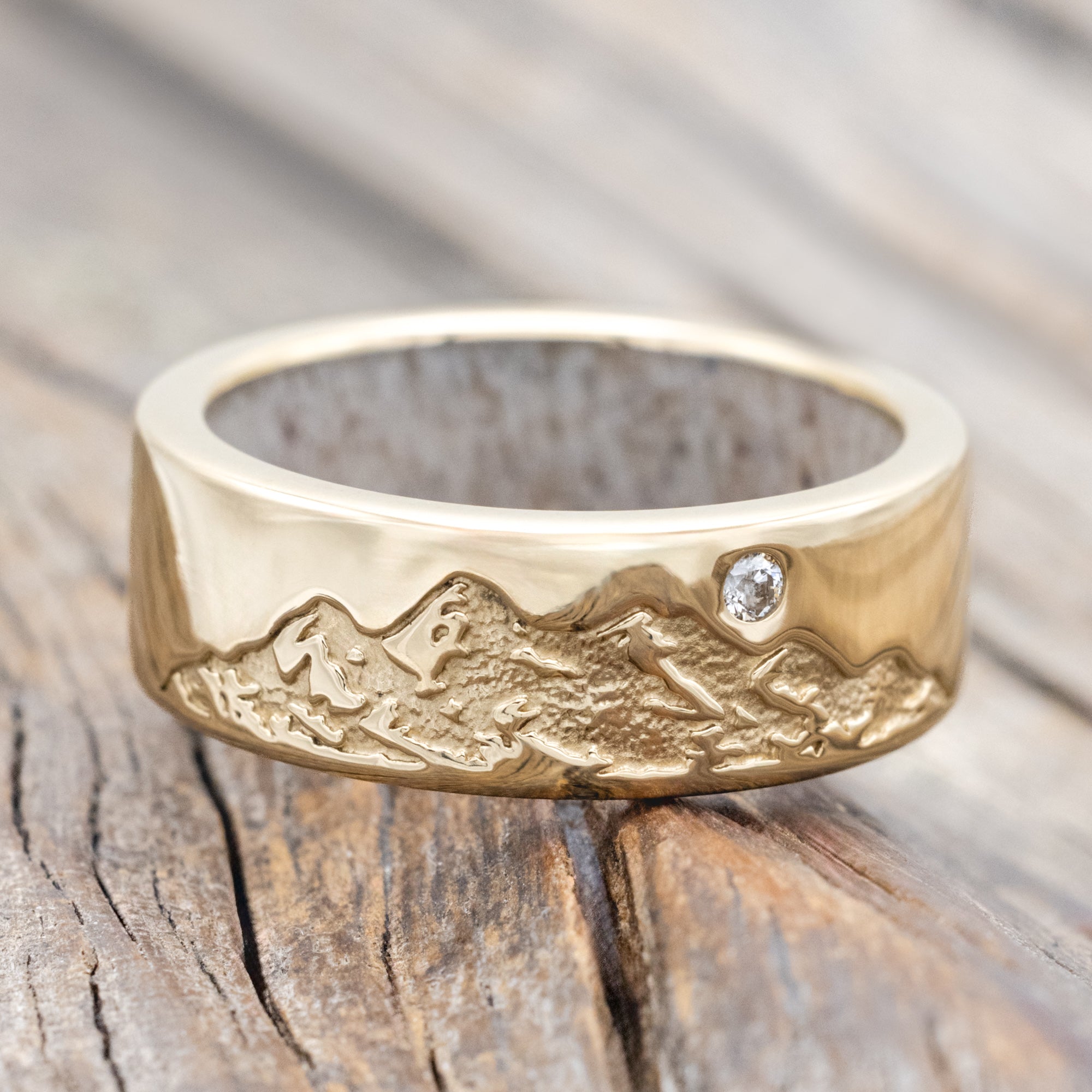 Gold ring with antler lining, diamond accent & mountain engraving on a wooden surface