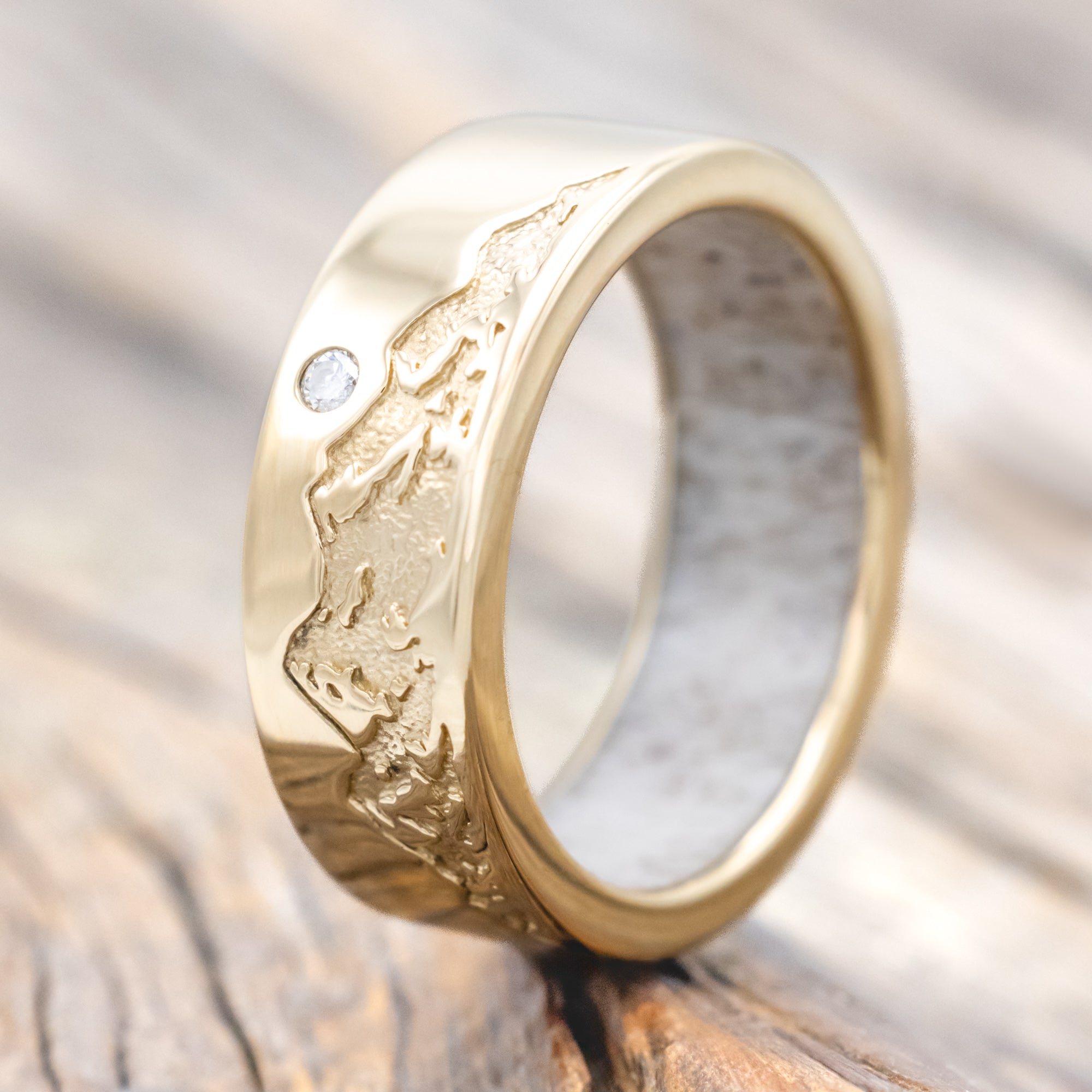 Gold ring with antler lining, diamond accent & mountain engraving on a wooden surface