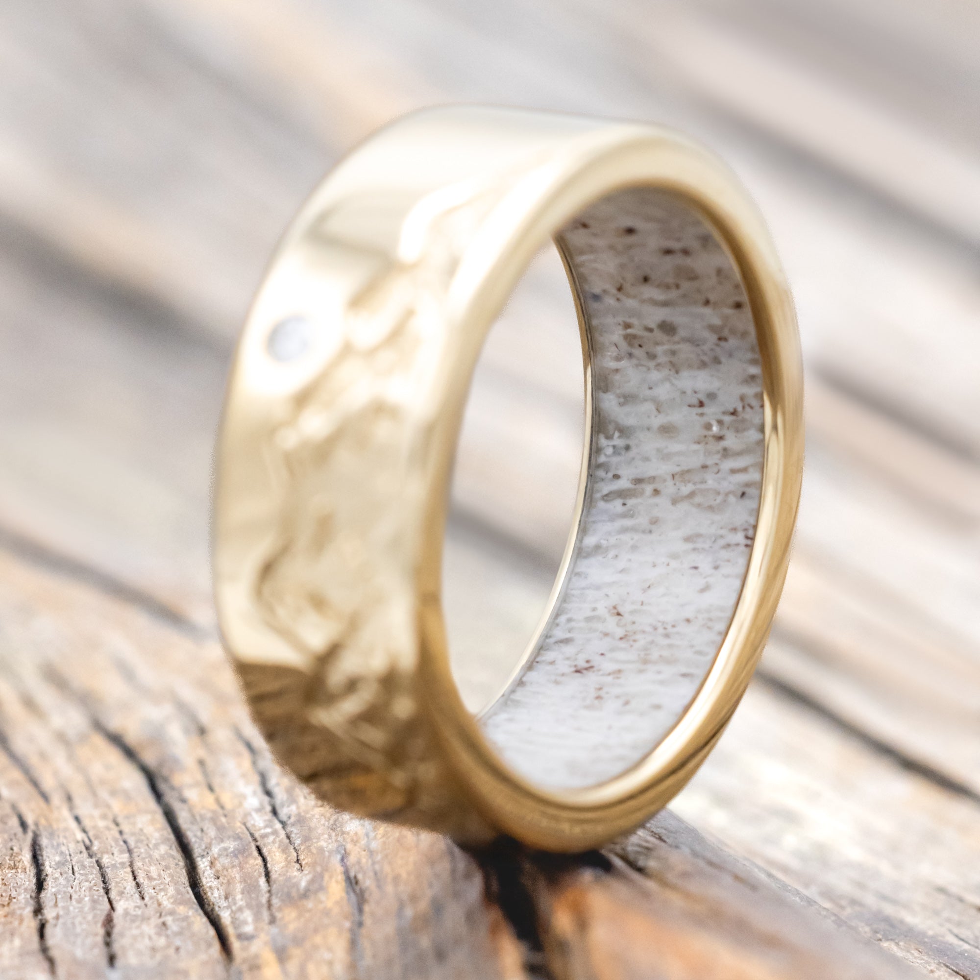Gold ring with antler lining, diamond accent & mountain engraving on a wooden surface