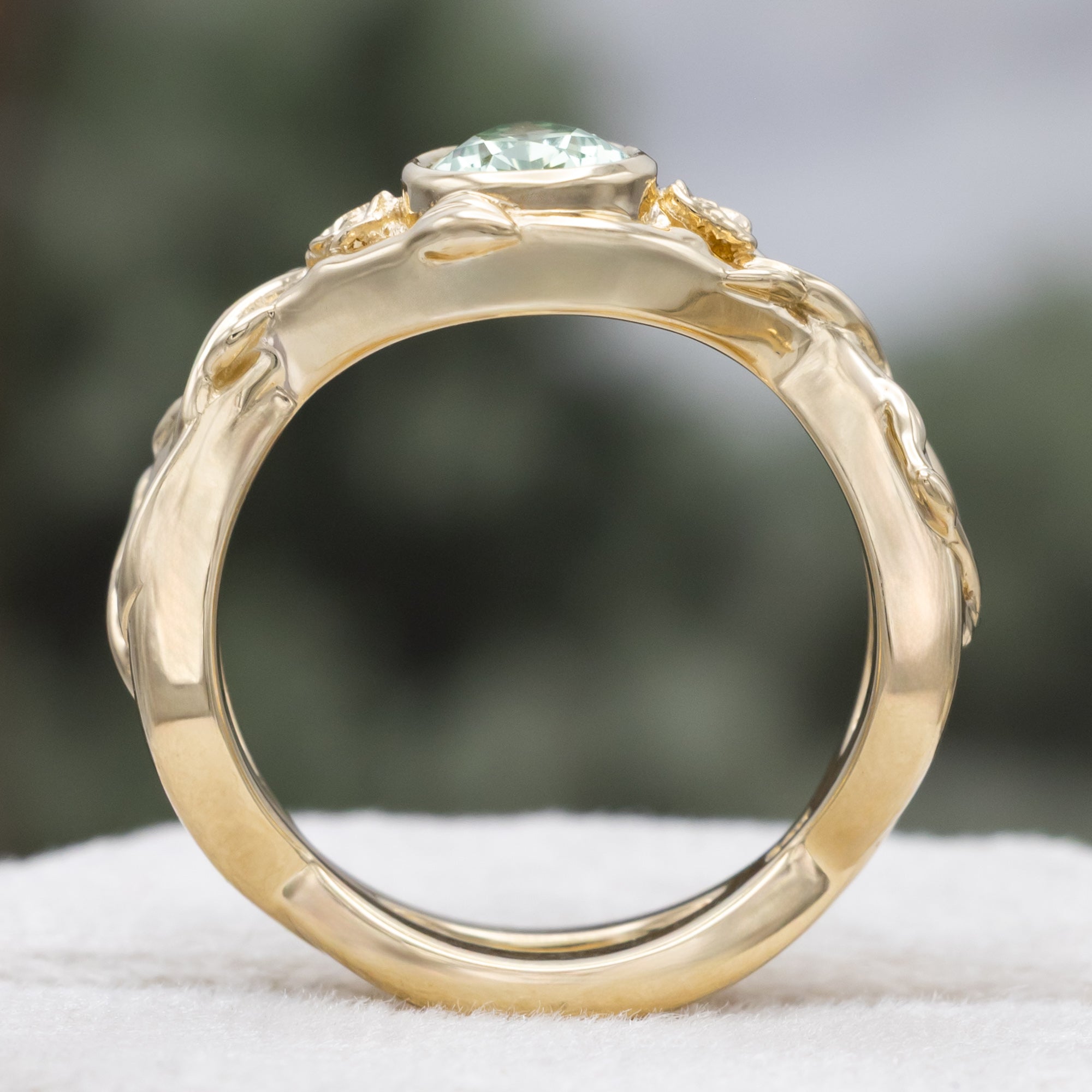 Gold ring with pear lab sapphire and rose/vine accents on a blurred background
