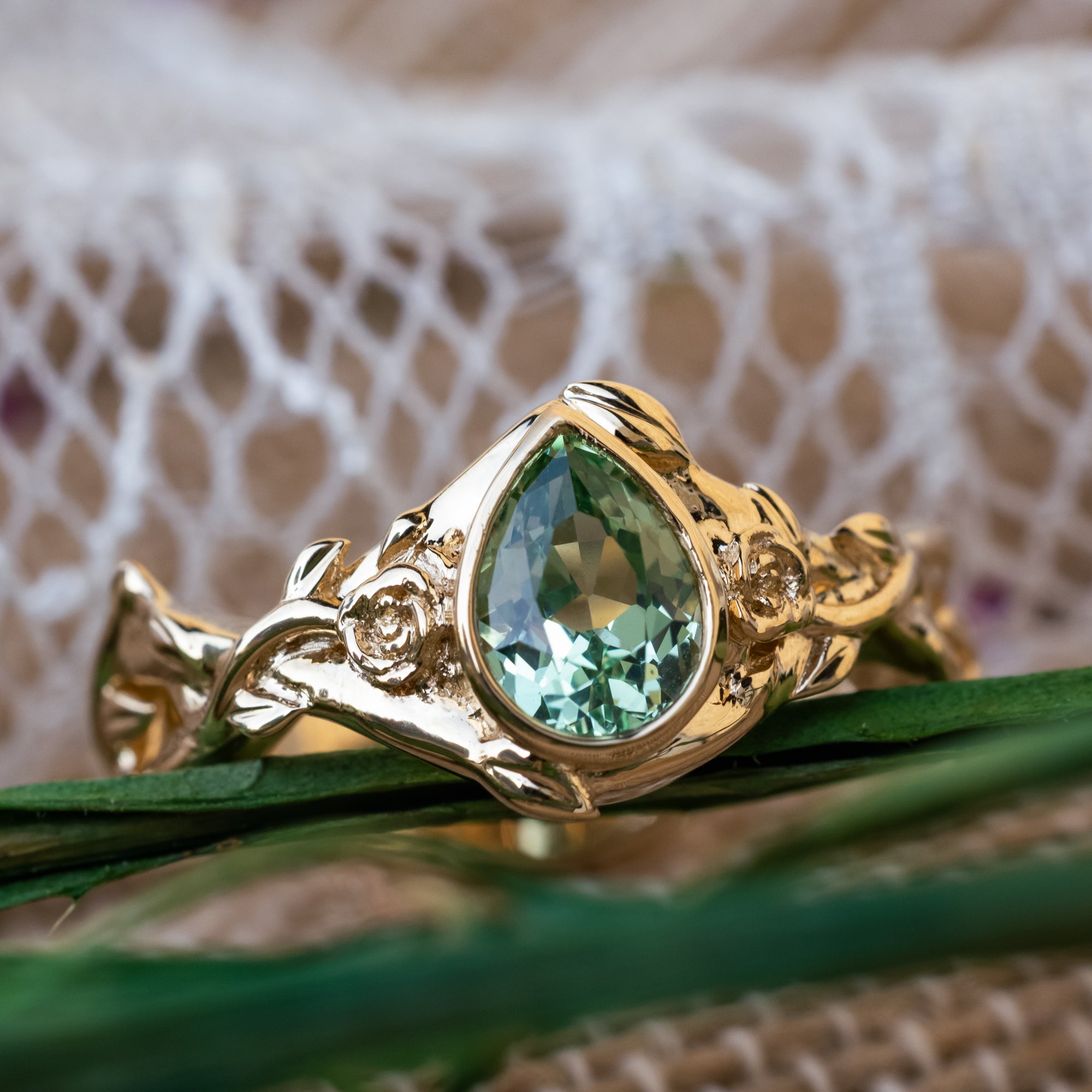 Gold ring with pear lab sapphire and rose/vine accents on a decorative background
