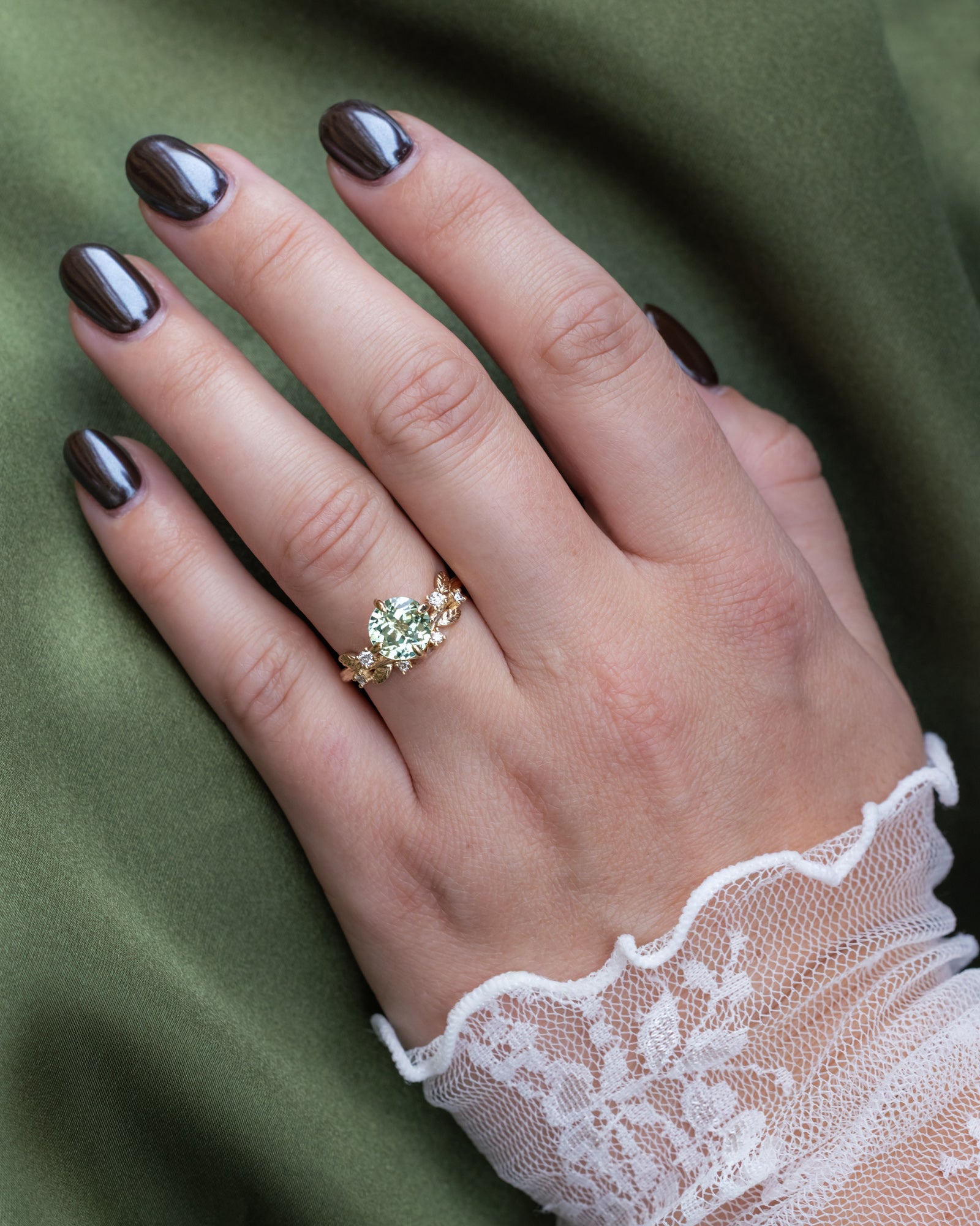 Hand wearing a gold ring with a green sapphire on a green fabric background