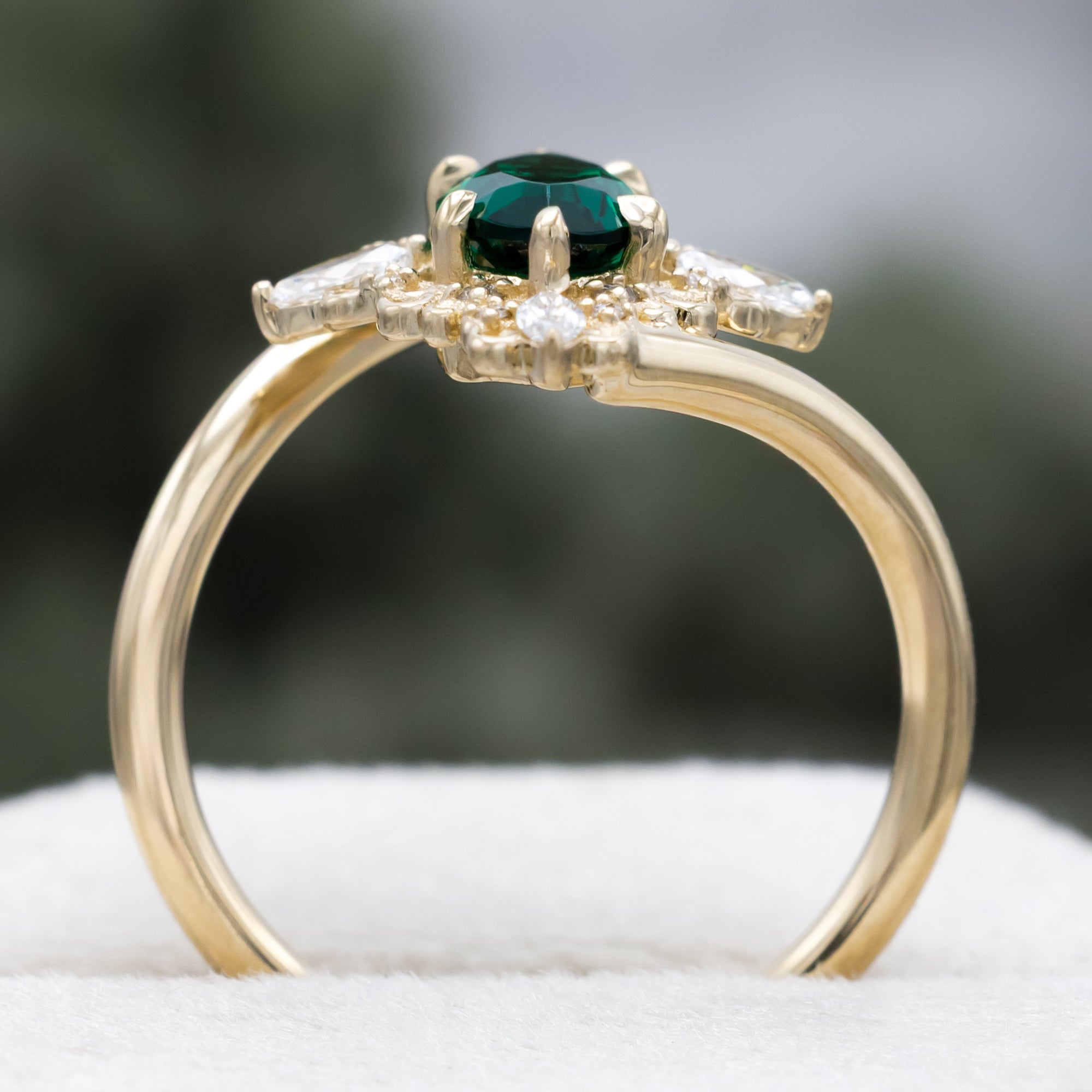 Gold ring with green emerald and diamond halo on a neutral background