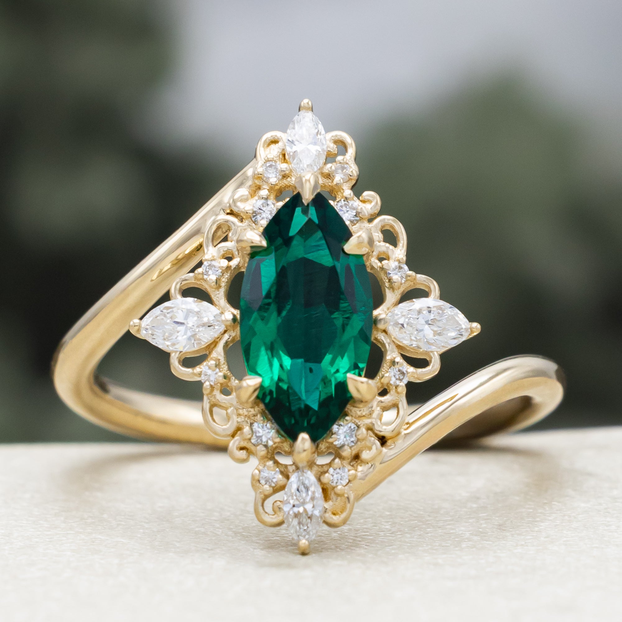 Gold ring with green emerald and diamond halo on a neutral background