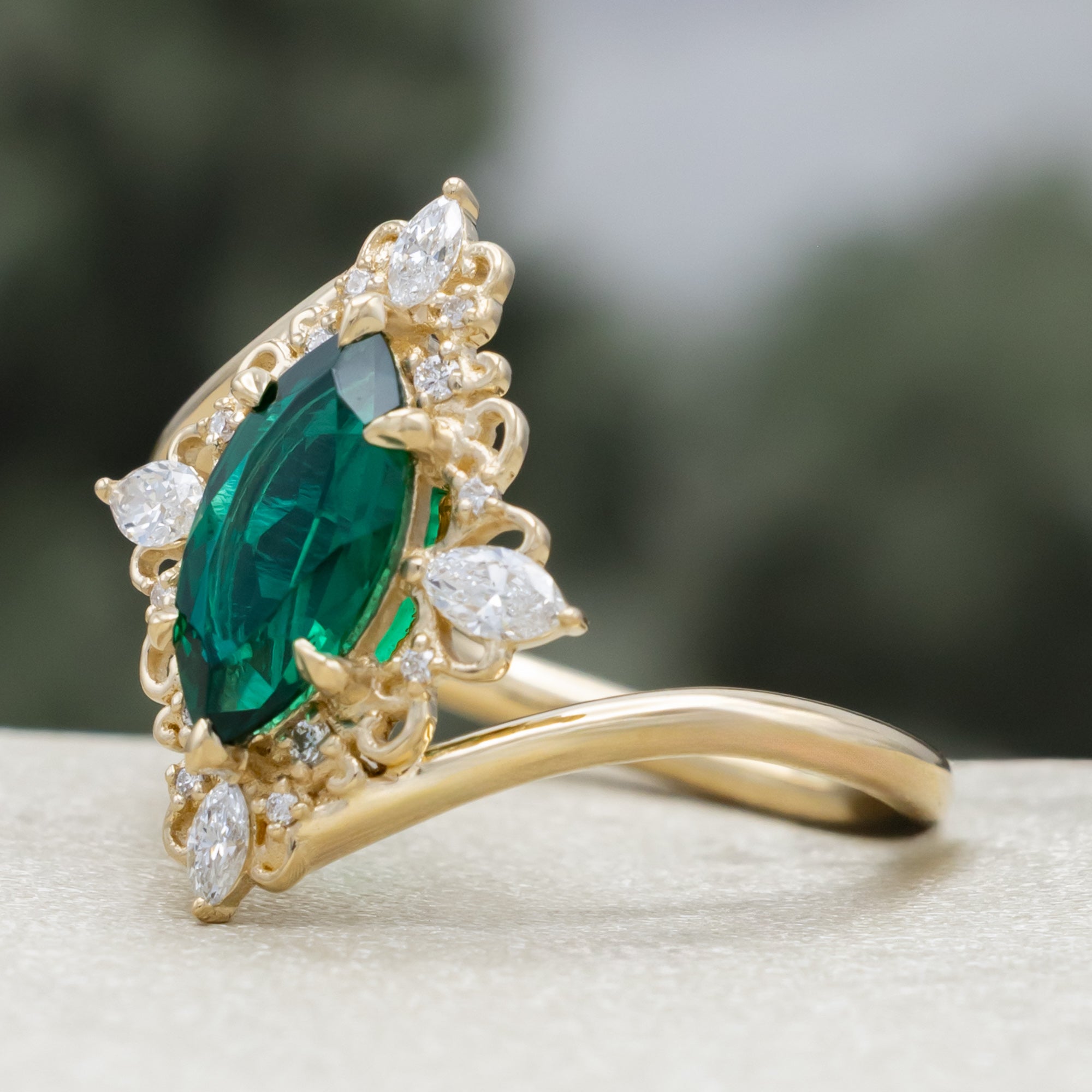 Gold ring with green emerald and diamond halo on a neutral background