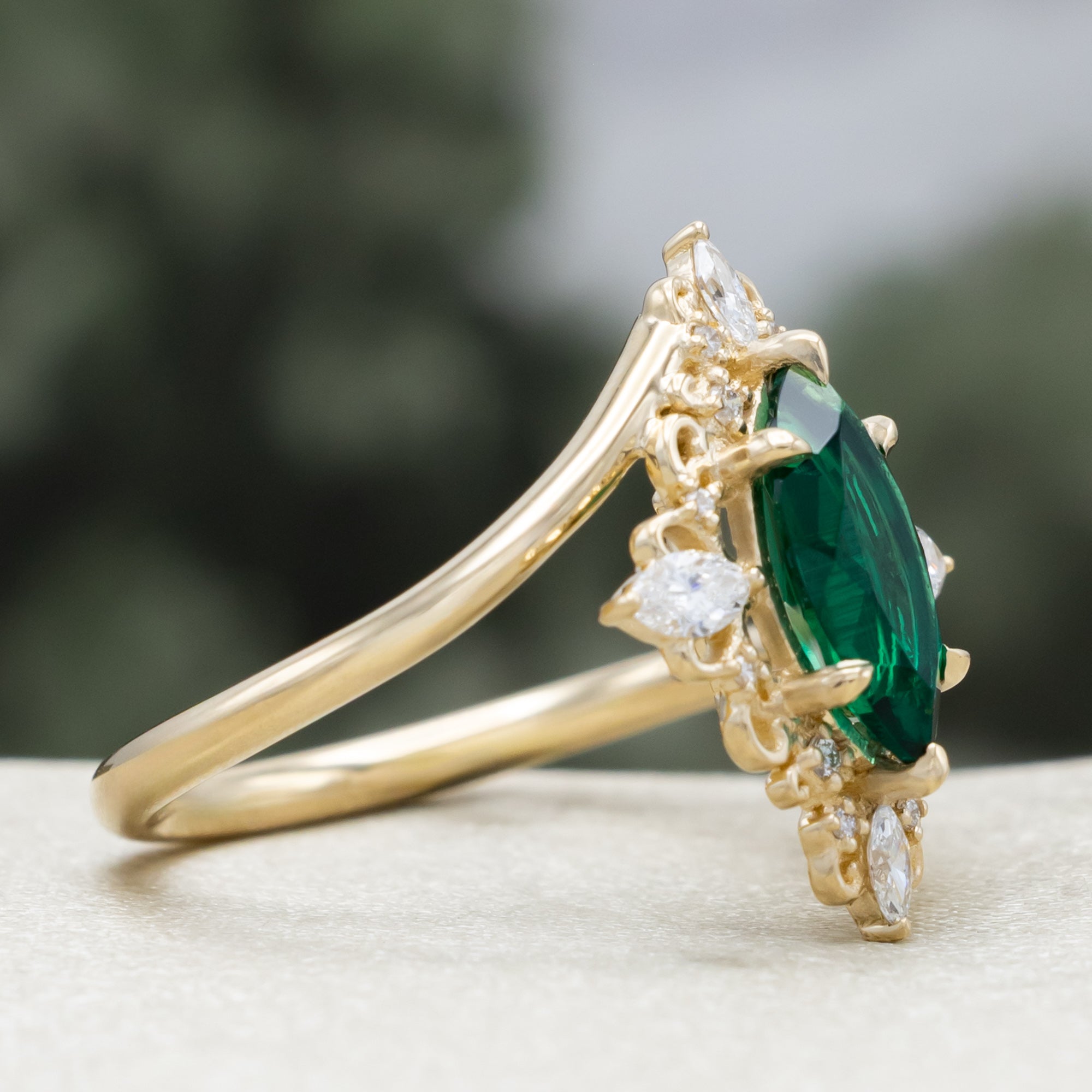 Gold ring with green emerald and diamond halo on a neutral background