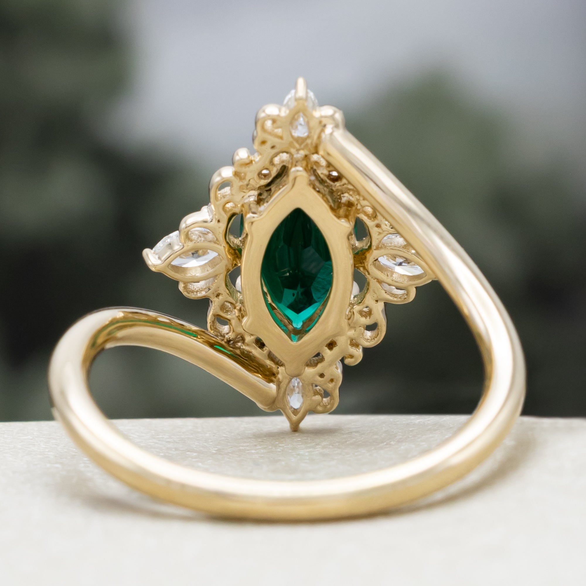 Gold ring with green emerald and diamond halo on a neutral background