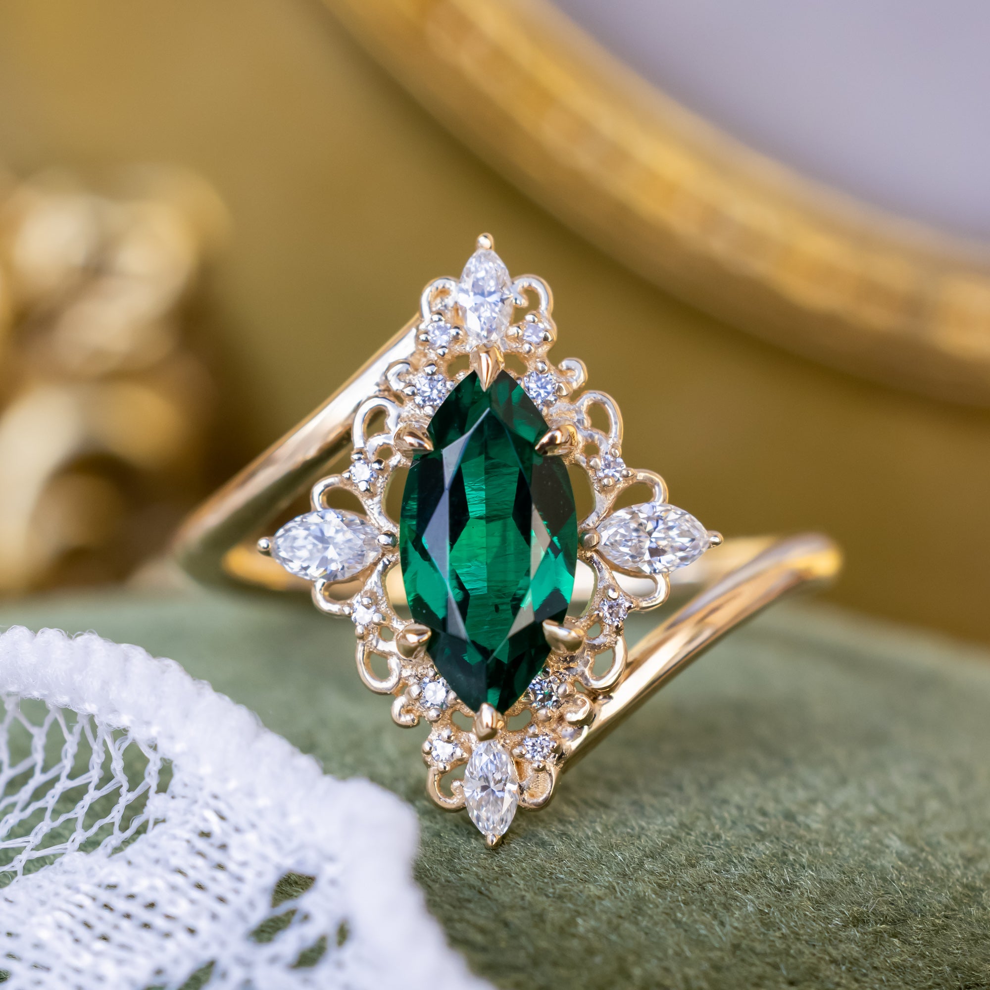 Gold ring with a marquise emerald and diamond accents on a green surface.