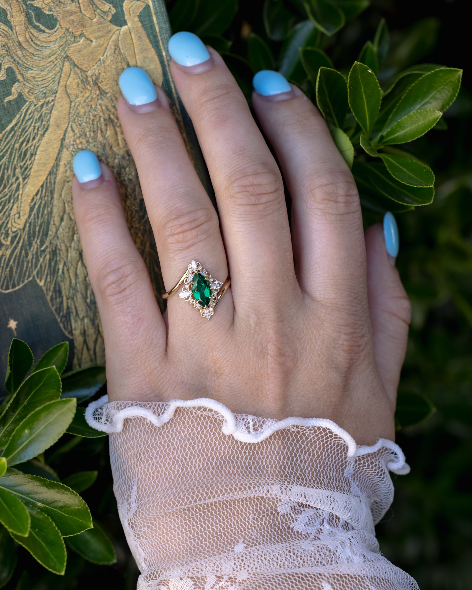 Hand wearing a ring with a green emerald against a leafy background