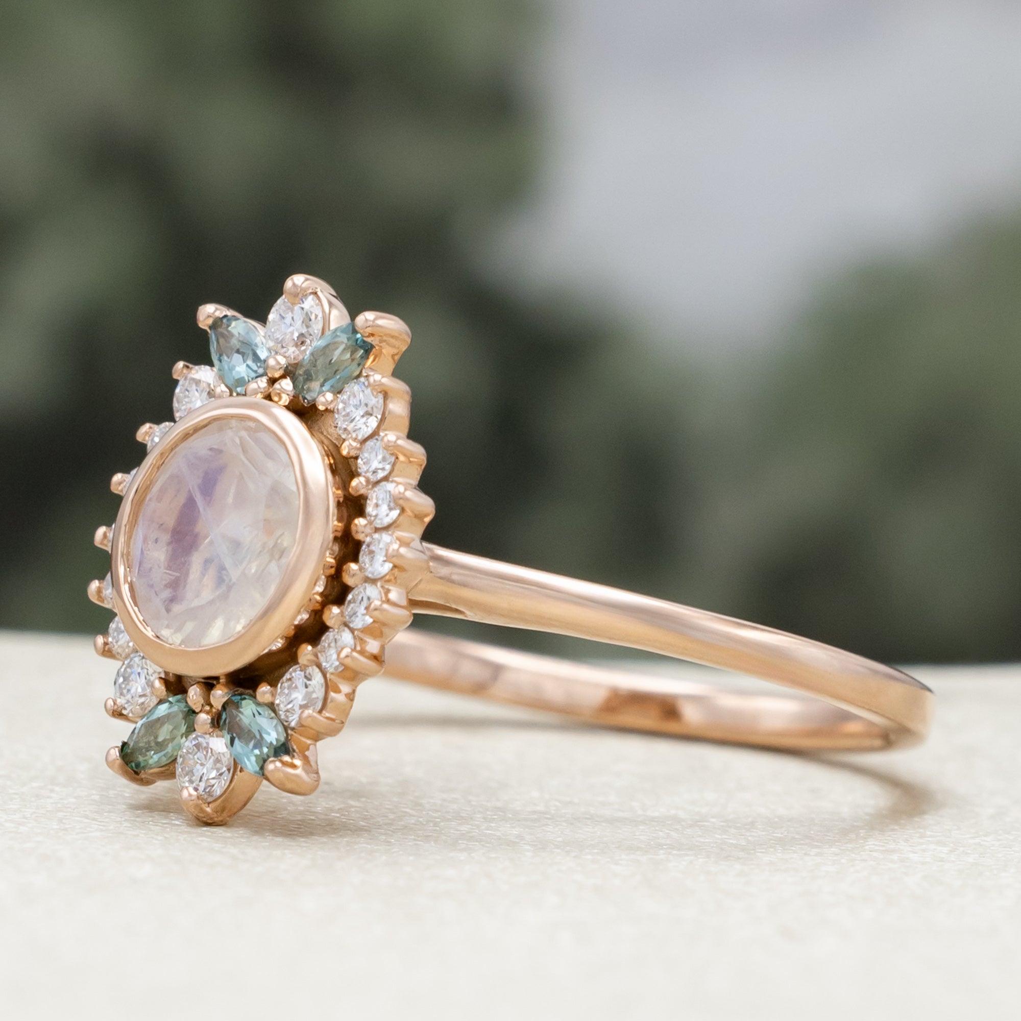 Rose gold ring with a central moonstone and gemstone accents on a neutral background