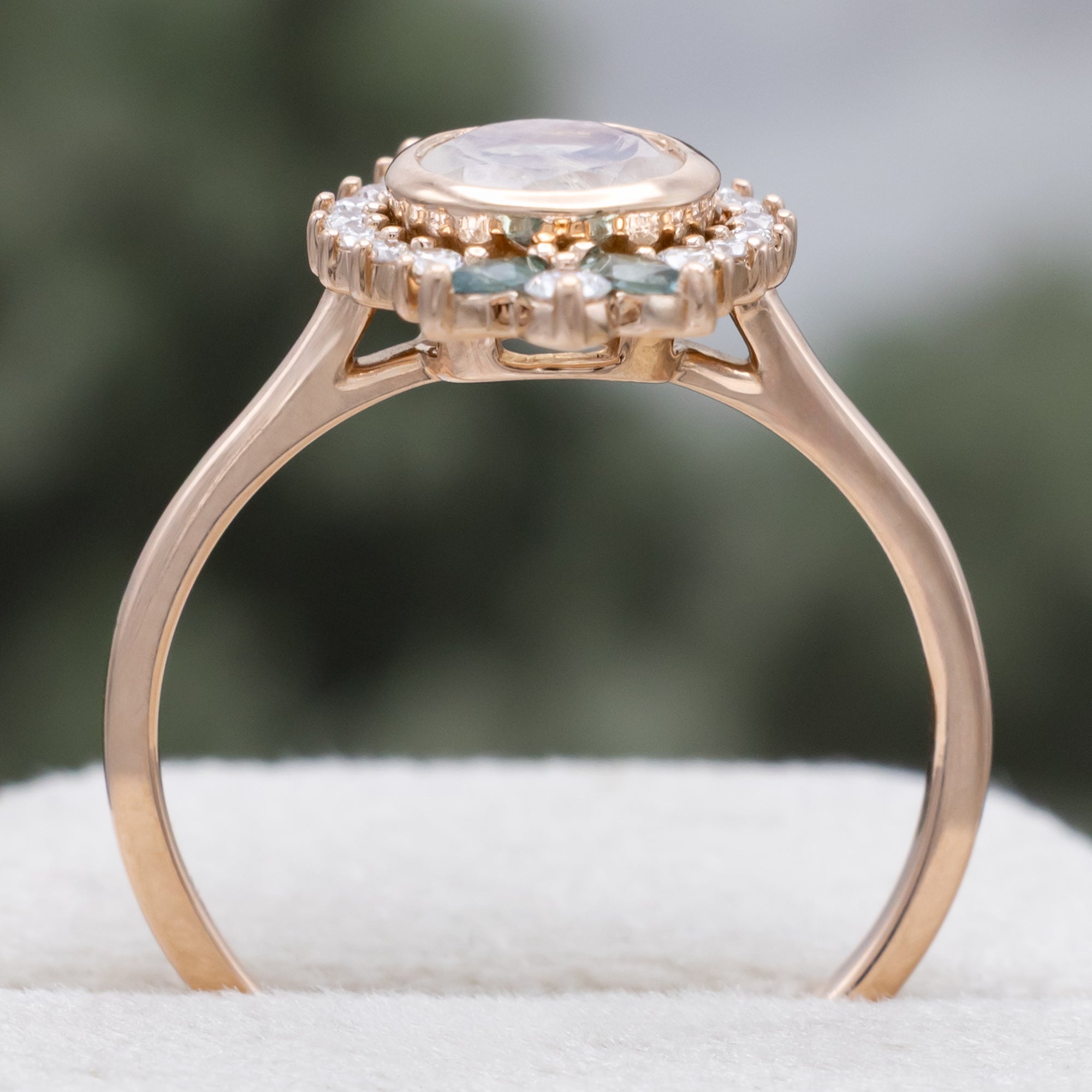 Rose gold ring with a central moonstone and gemstone accents on a neutral background