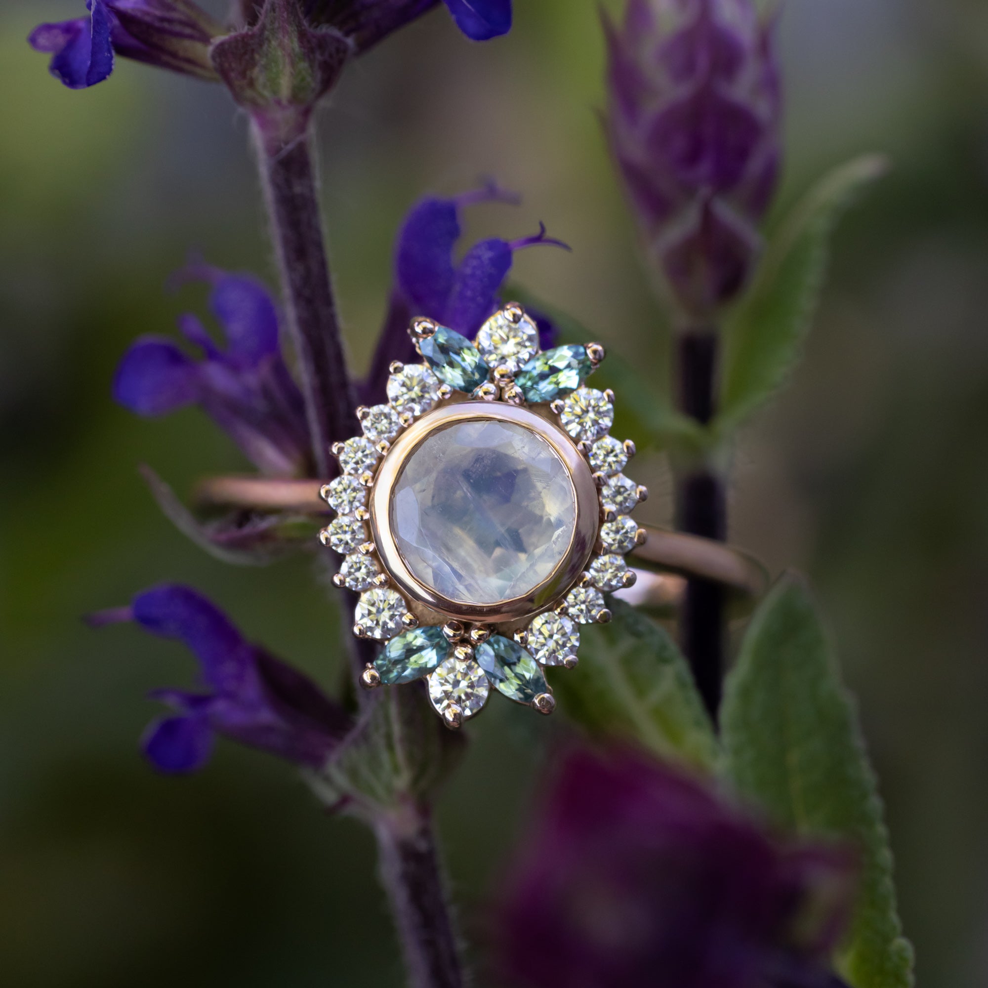 rose gold ring with round moonstone and gemstone accents with purple flowers in the background