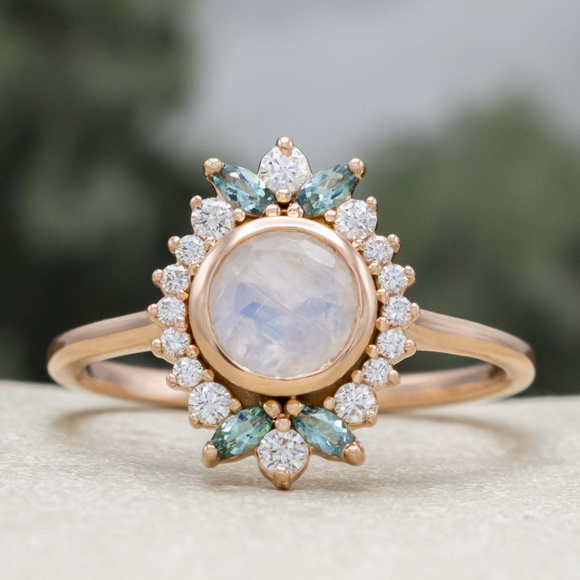 Rose gold ring with a central moonstone and gemstone accents on a neutral background