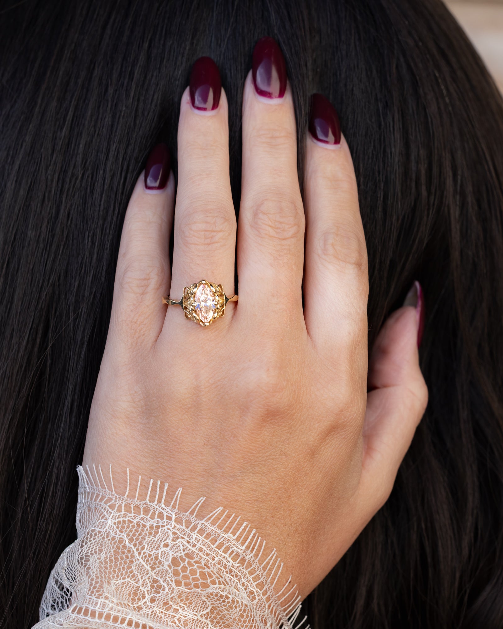 Hand wearing a gold ring with a pink diamond, set against a dark background