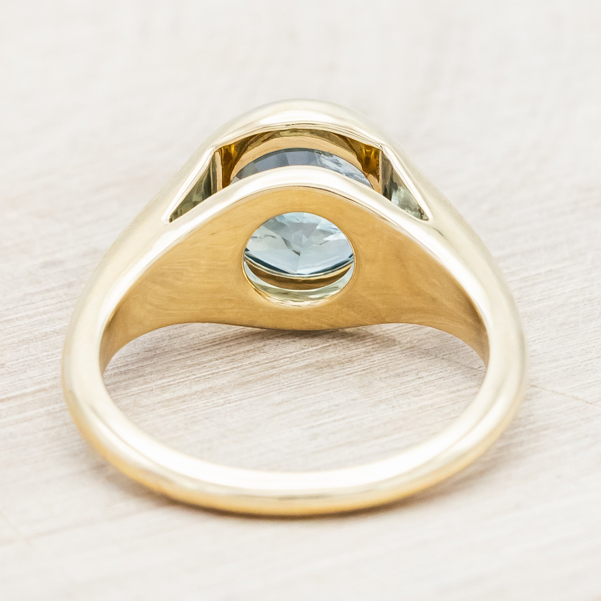 Yellow gold ring with a blue Montana sapphire against a wooden background
