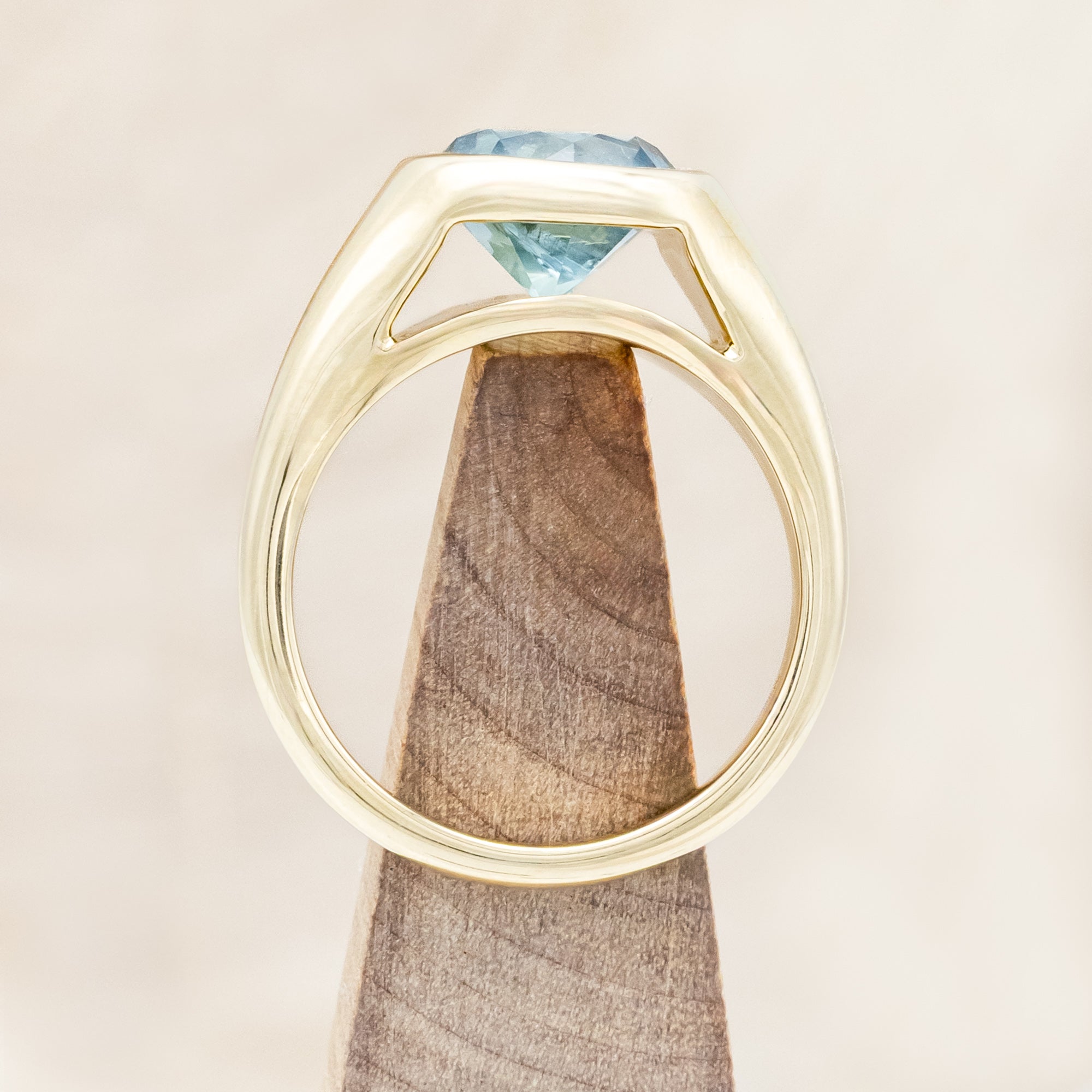 Yellow gold ring with a Montana sapphire on a wooden stand against a beige background