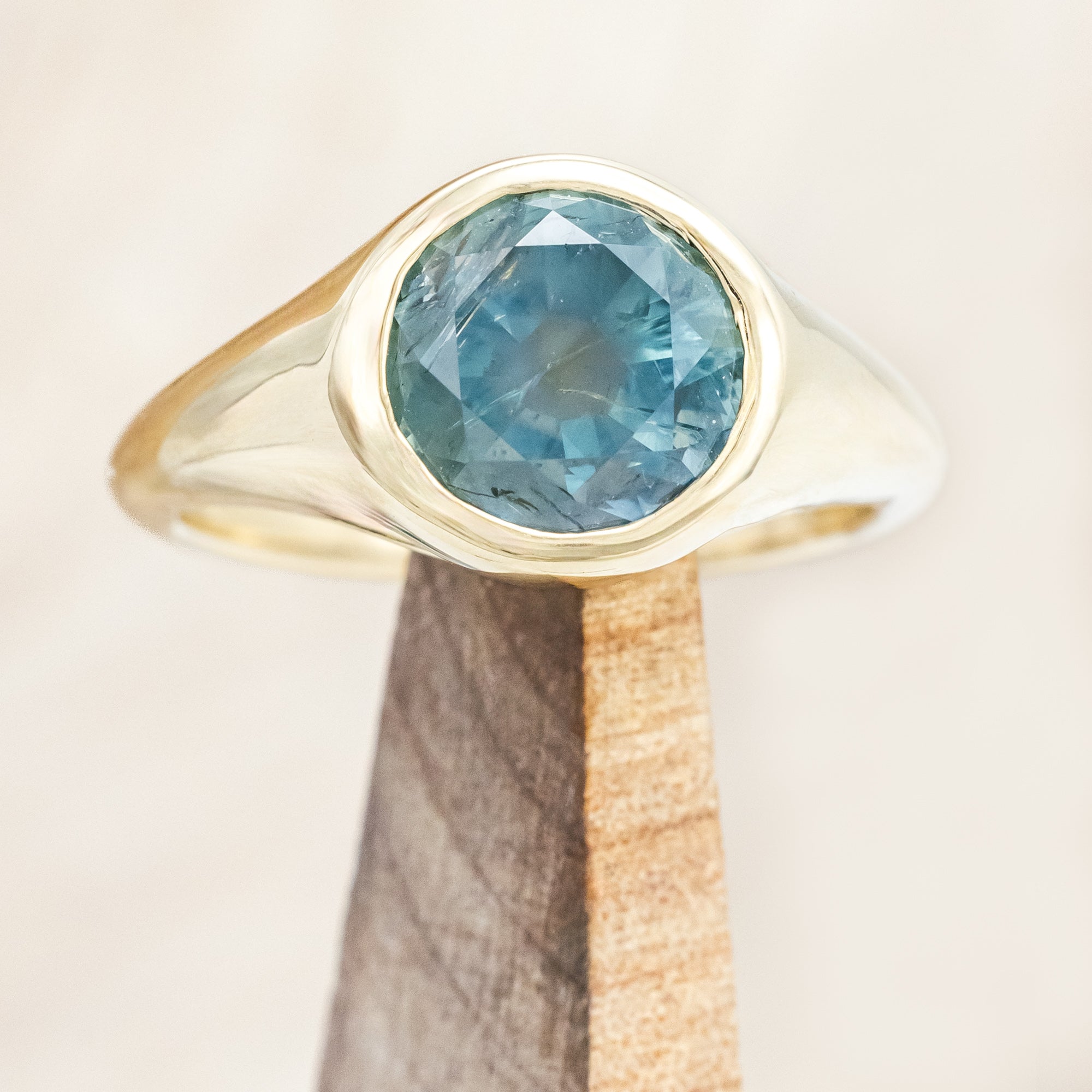Yellow gold ring with a blue Montana sapphire on a wooden stand against a beige background