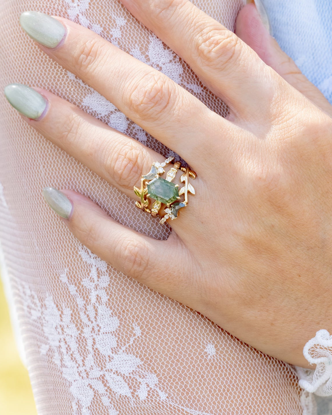 Hand wearing a gold ring with moss agate on lace fabric