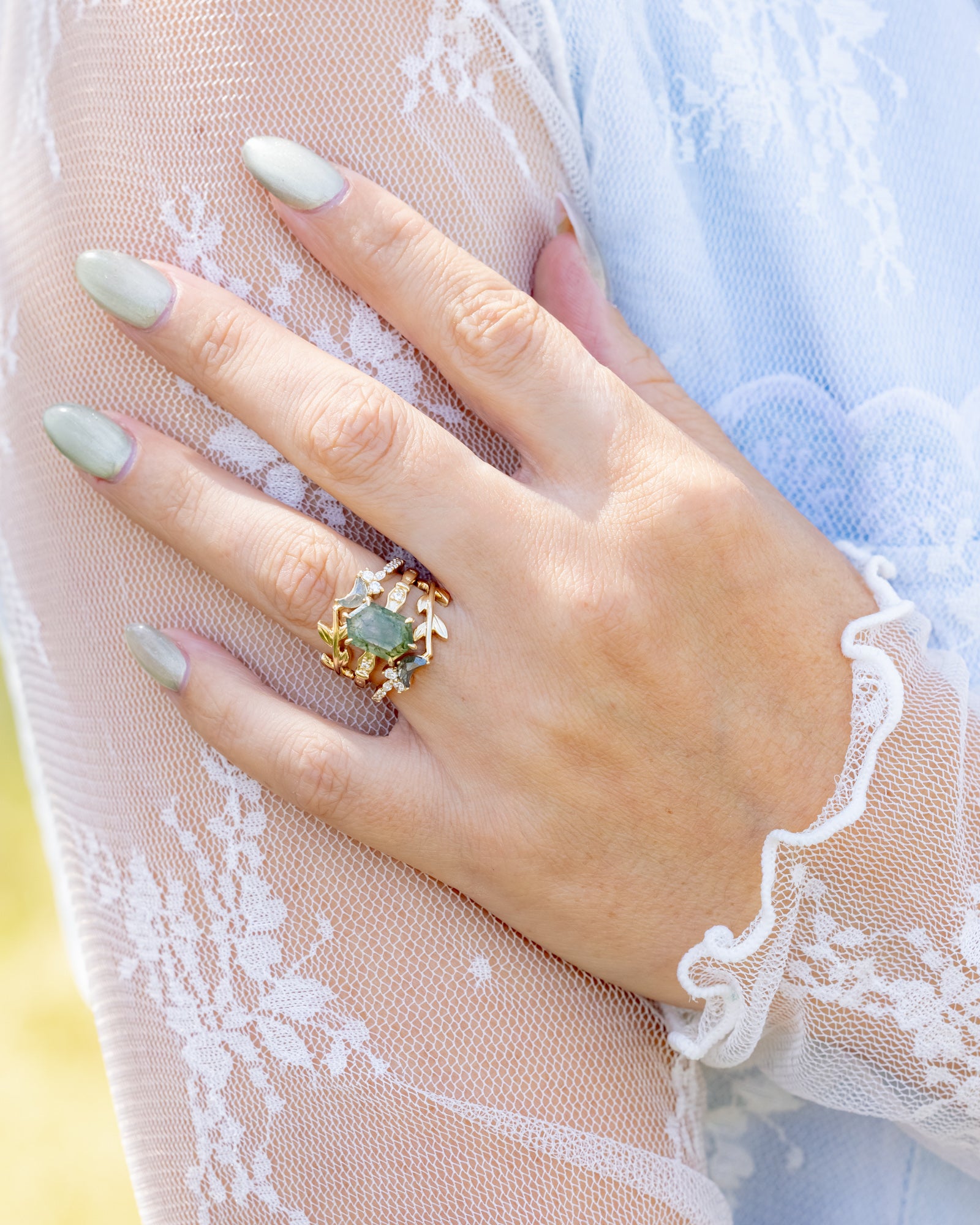 Hand wearing a gold ring with moss agate on lace fabric