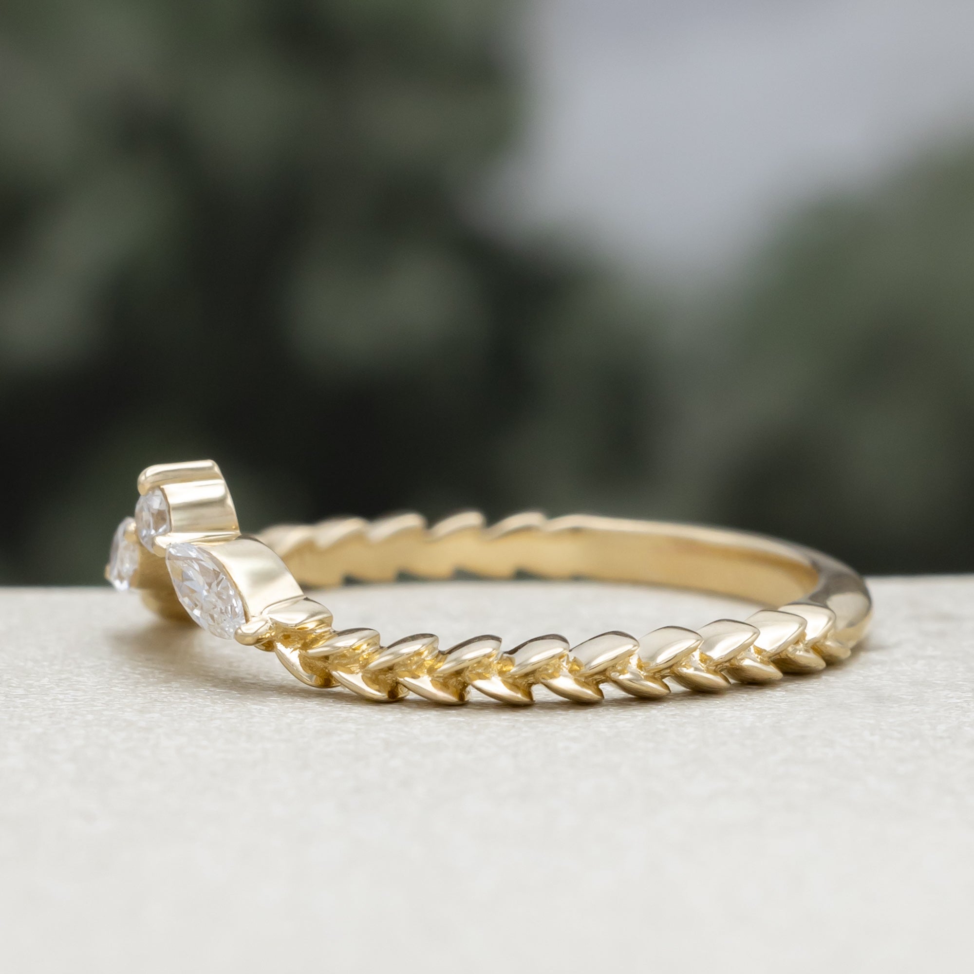 A yellow gold ring tracer with three diamond accents on a vine style band against a blurred green background